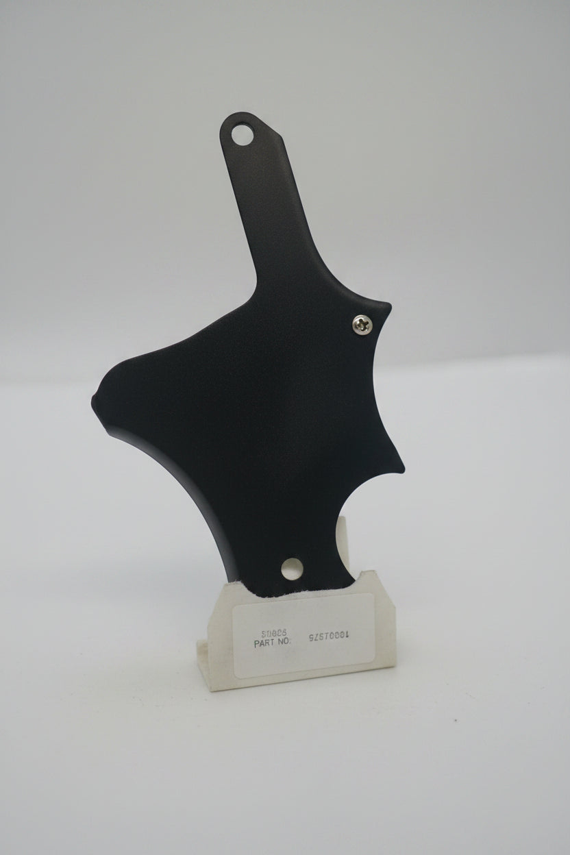 A close-up, slightly blurry shot of a black leather or faux-leather strap or holster with silver rivets, mounted against a plain light gray or off-white background.