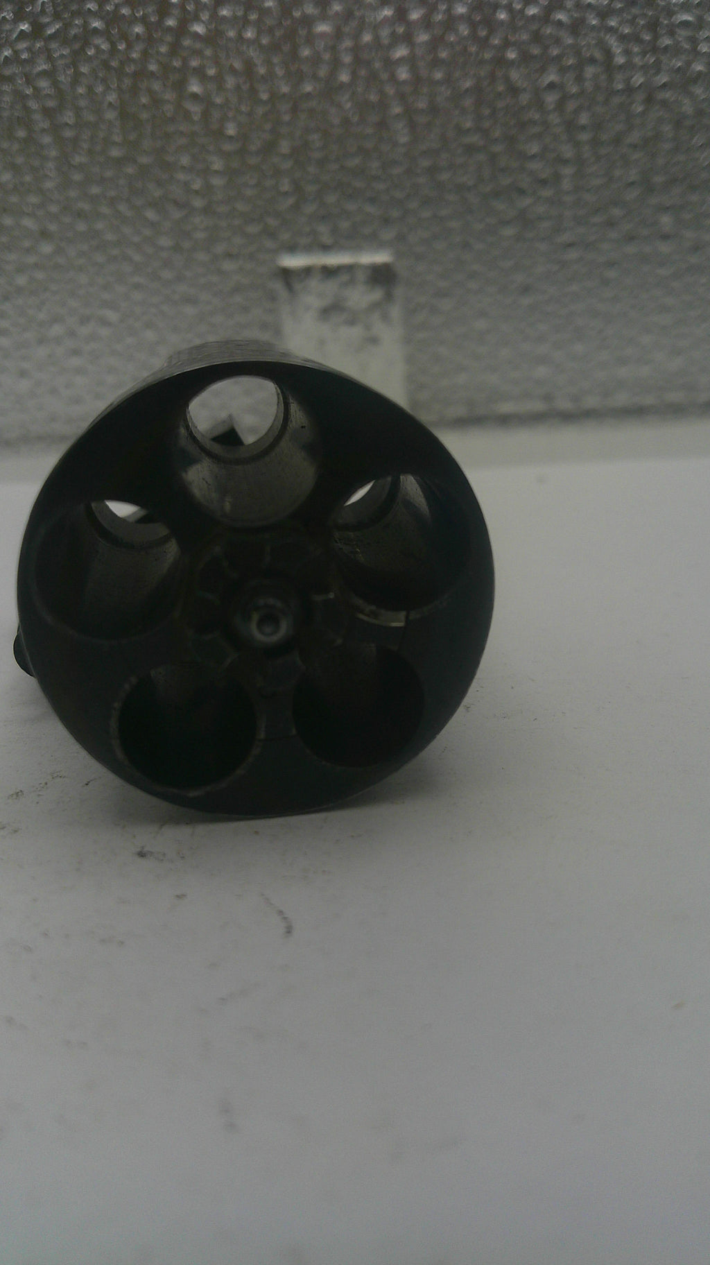Black cylindrical object with multiple holes on a textured surface