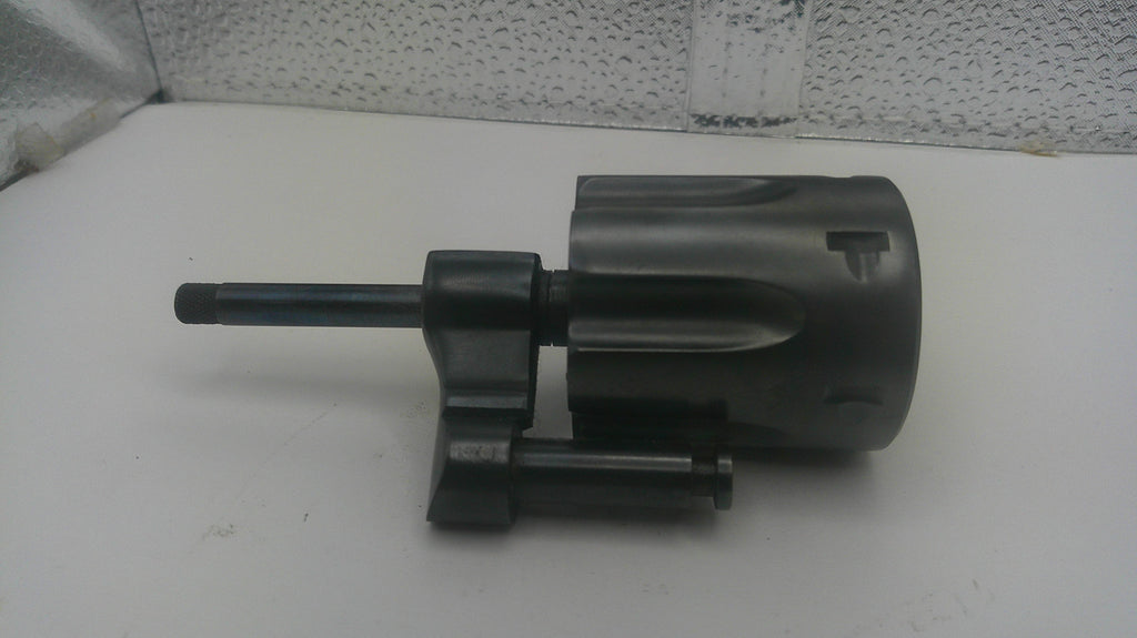 A dark gray and black cylindrical mechanical part with a protruding rod, photographed on a white surface against a textured light gray backdrop.