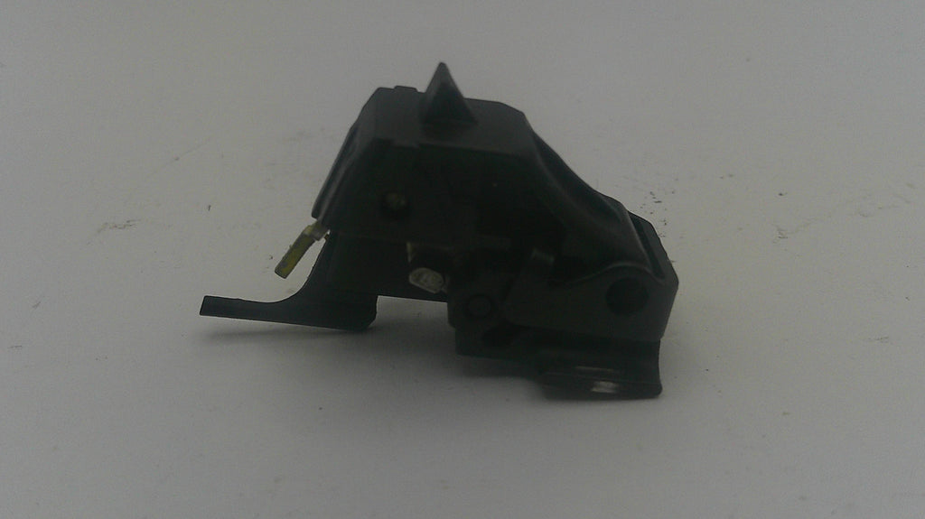 A small black plastic mechanical part with a pointed top and a short protruding tab, photographed on a plain light gray surface.