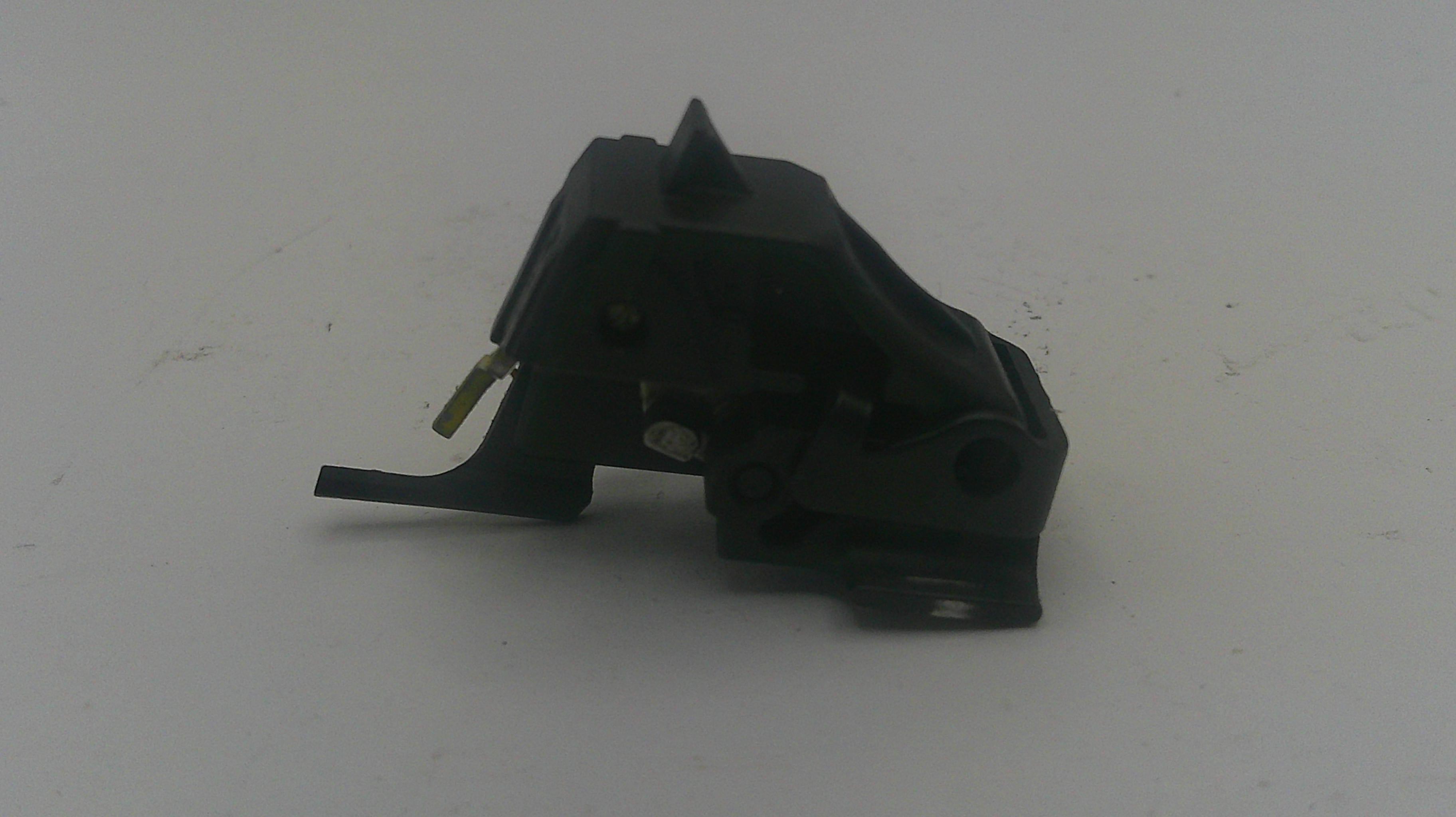 A small black plastic mechanical part with a pointed top and a short protruding tab, photographed on a plain light gray surface.