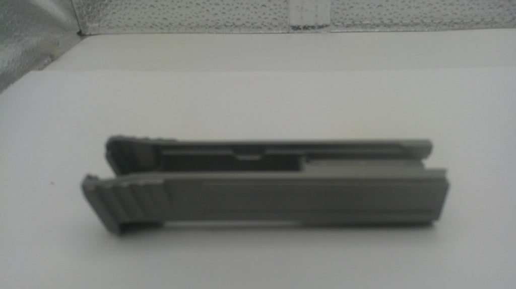 A dark gray plastic replacement part, possibly a clip or bracket, shown from a side profile on a white surface.