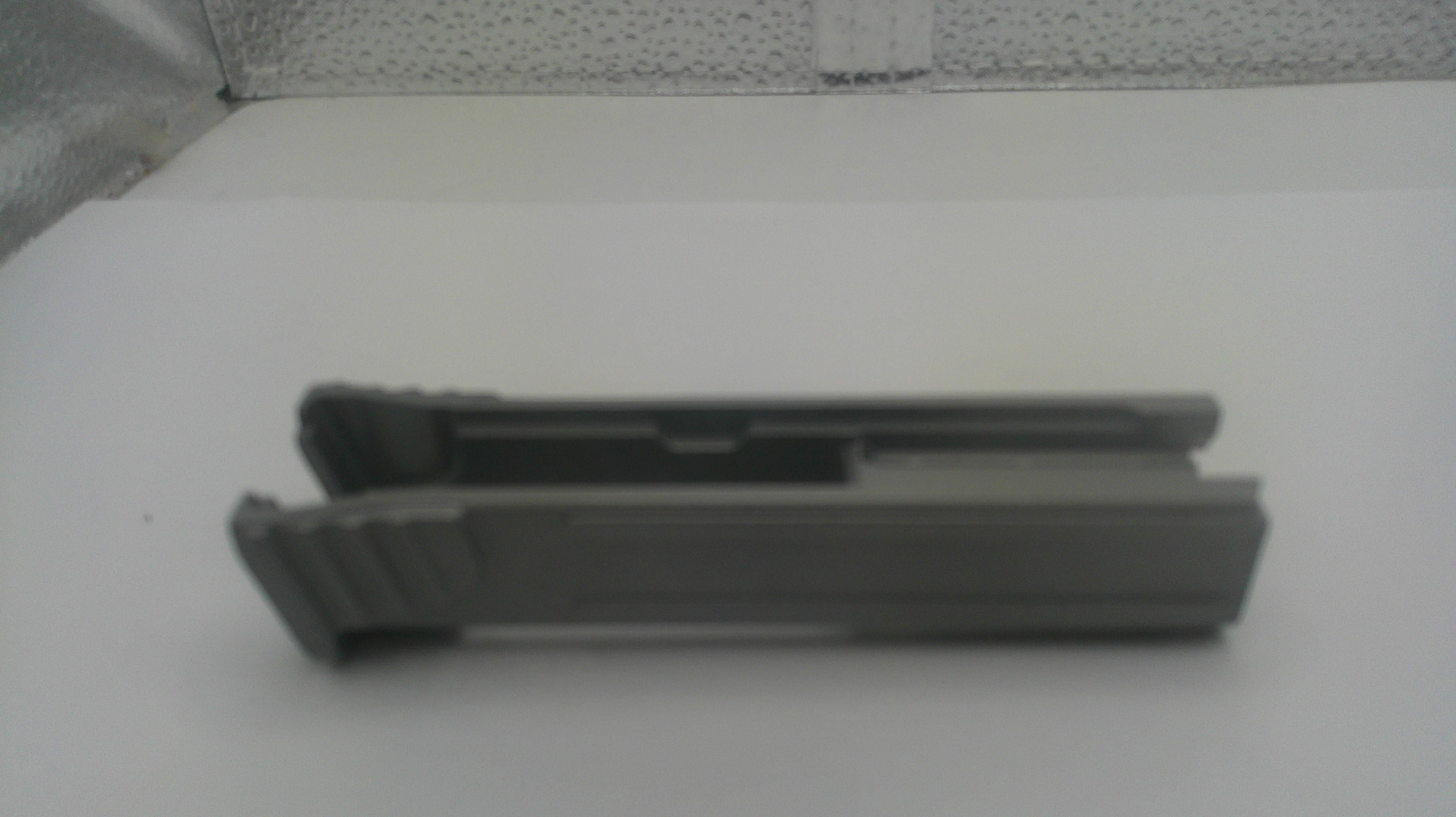 A dark gray plastic replacement part, possibly a clip or bracket, shown from a side profile on a white surface.