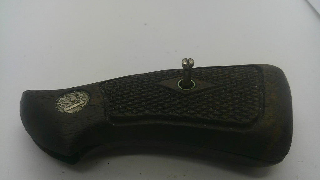 A close-up of a dark brown wooden object with a textured grip pattern, a small silver metal knob on top, and a circular silver emblem on the left side, photographed against a plain light background.