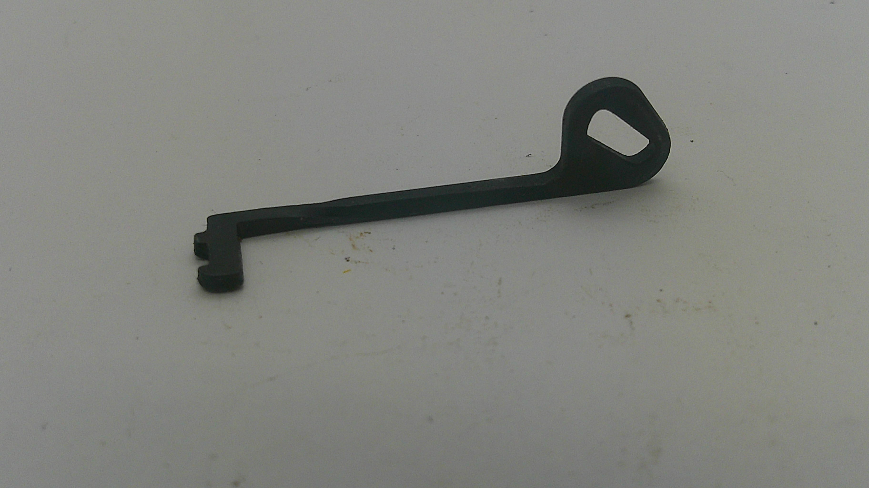 A small black plastic or metal key-shaped tool with a loop at one end, placed on a plain off-white surface.