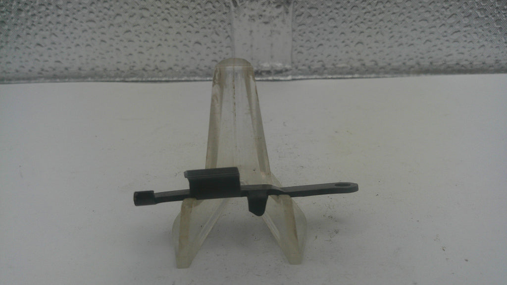 A small black plastic or metal tool with a curved flat bar and a short perpendicular arm, displayed on a clear plastic stand against a light gray textured background.