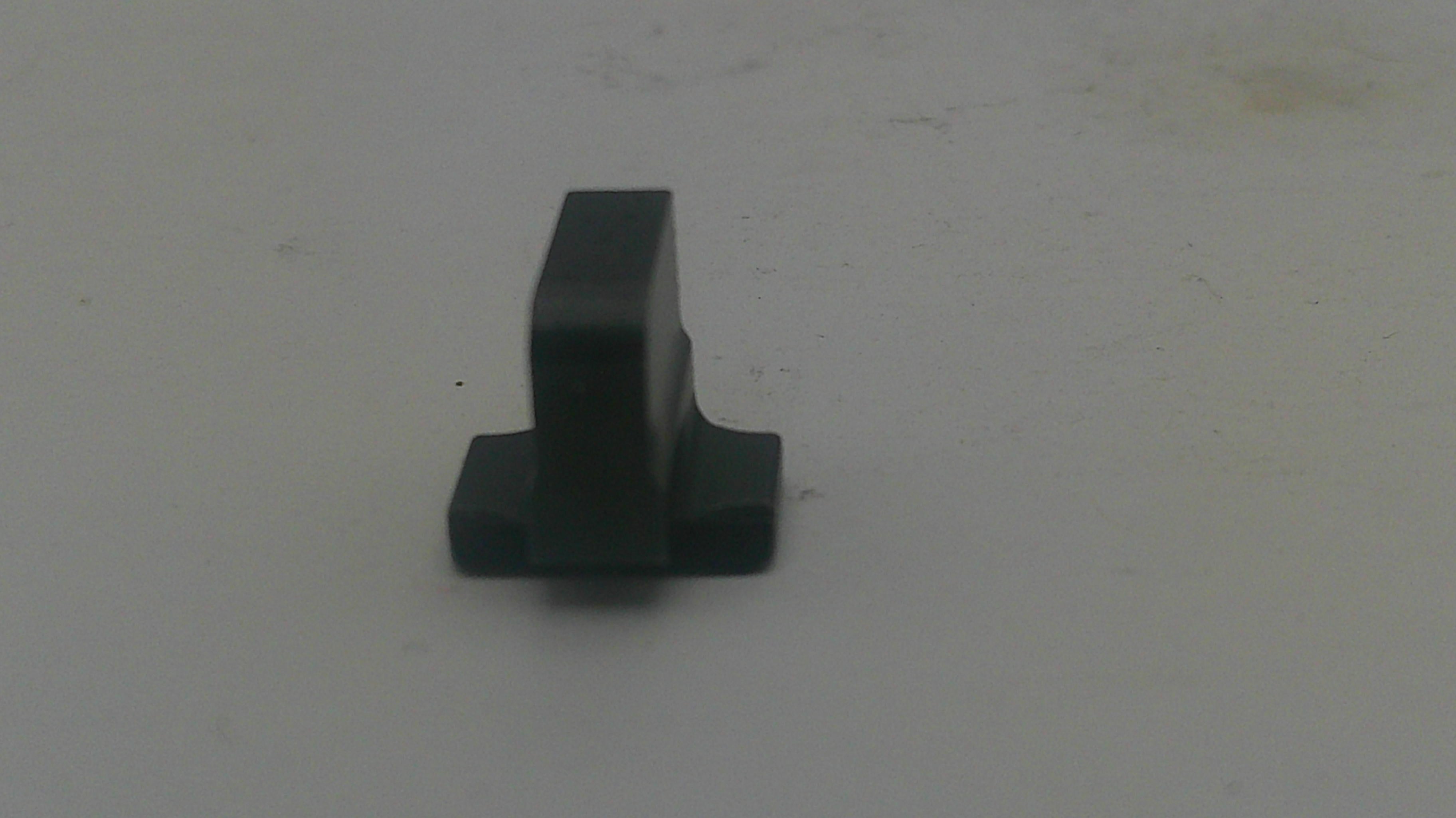 A small black plastic hardware component, possibly a latch stopper or mounting tab, shown on a plain light gray surface.