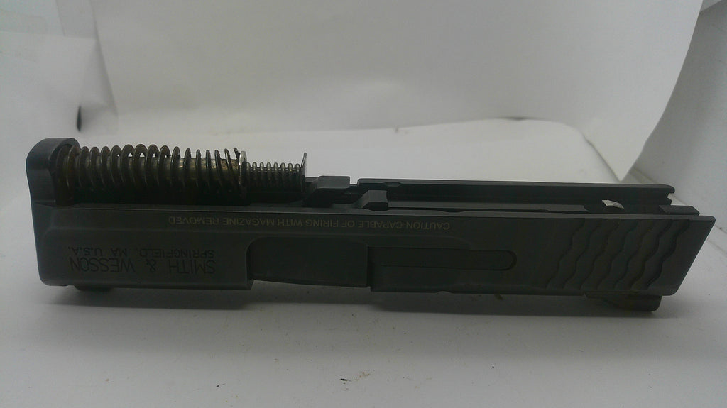 A black metal firearm magazine frame or receiver component with a visible coiled spring, photographed on a plain white background.