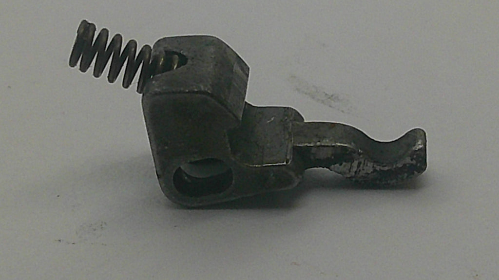 A small dark metal mechanical component with a coiled spring and hook-like arm, photographed on a plain light gray background.