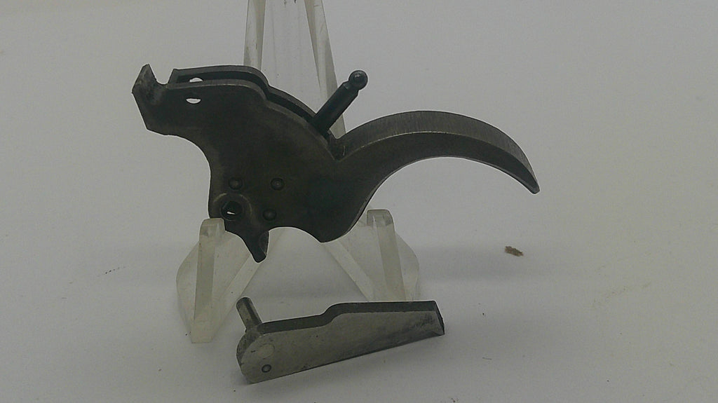 A dark metal trigger assembly with a curved trigger guard and a separate metal component, displayed on clear plastic stands against a plain light background.