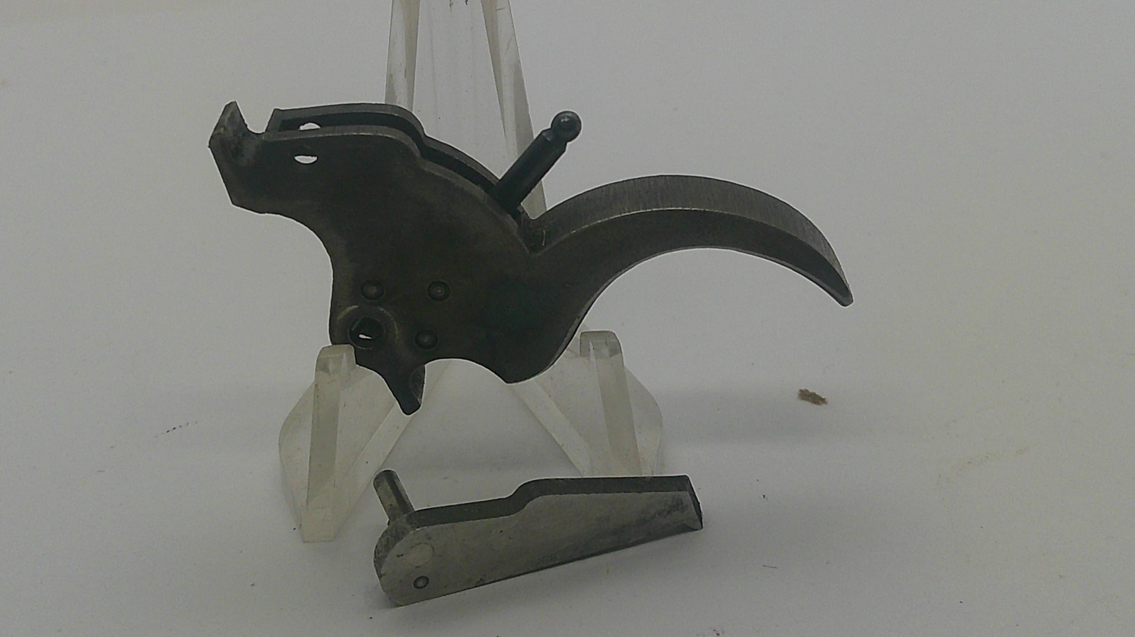A dark metal trigger assembly with a curved trigger guard and a separate metal component, displayed on clear plastic stands against a plain light background.