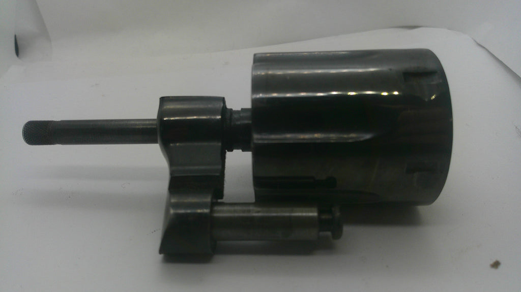 A dark metallic mechanical component with a cylindrical body, a short protruding rod, and a smaller attached rod, photographed on a plain light background.