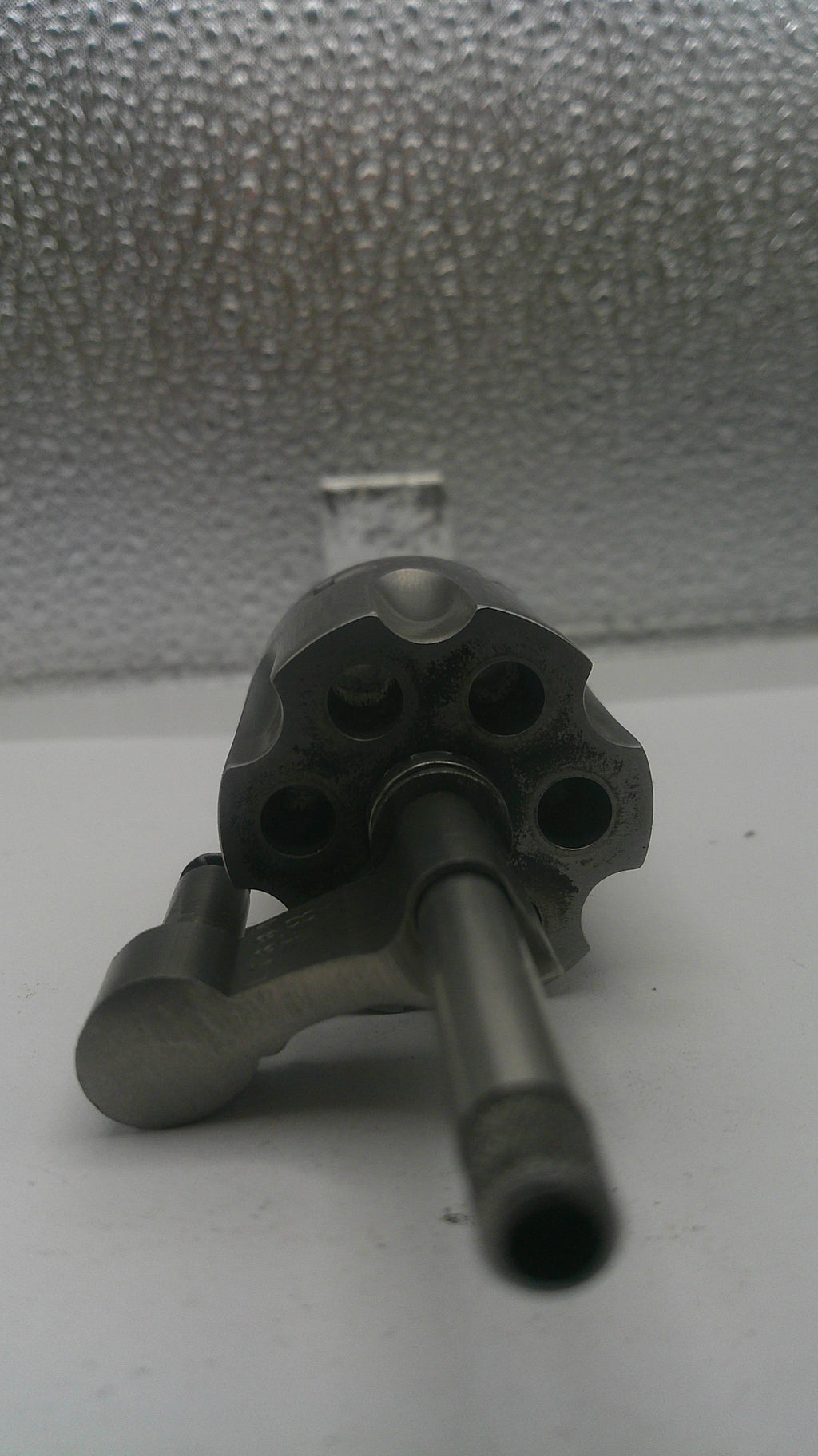 Metallic cylindrical object with multiple holes on a textured wall.