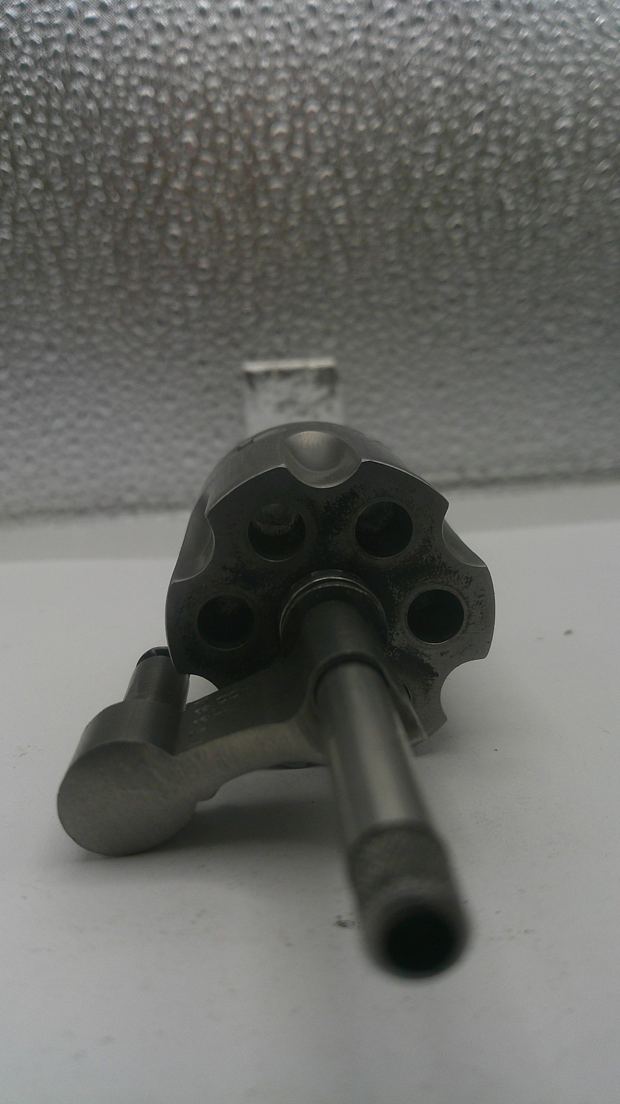 Metallic cylindrical object with multiple holes on a textured wall.