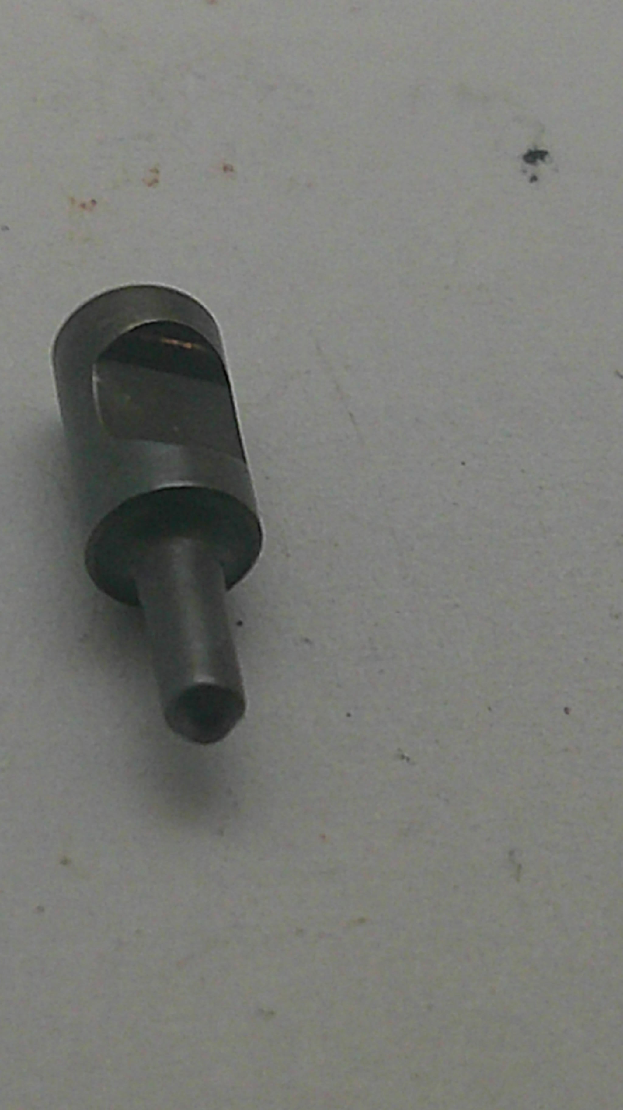A small dark metallic cylindrical tool or pin with a slotted side, photographed on a plain light gray surface.