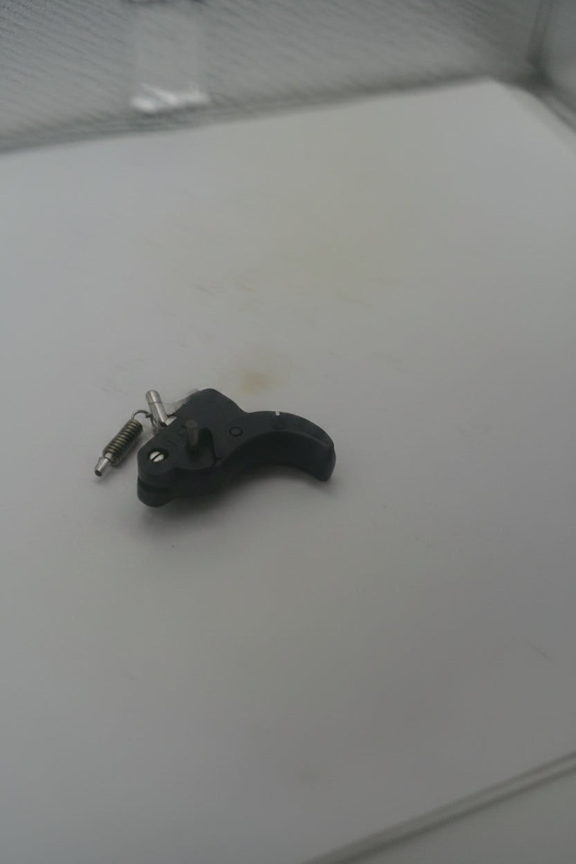 A close-up shot of a black plastic trigger lock or latch mechanism attached to a white surface.