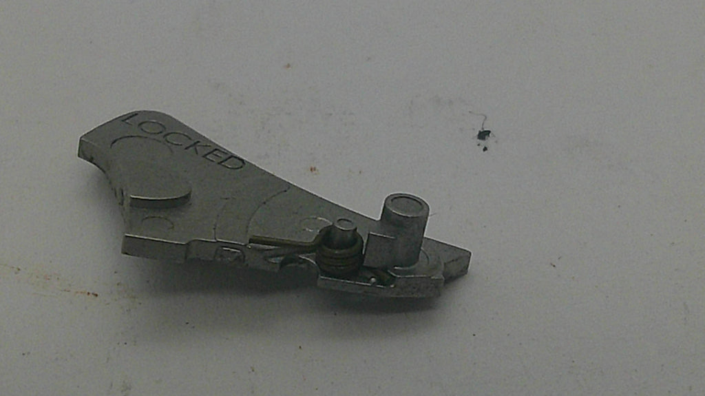 A small metallic mechanical part with the word 'LOCKED' printed on it, photographed on a plain light surface.