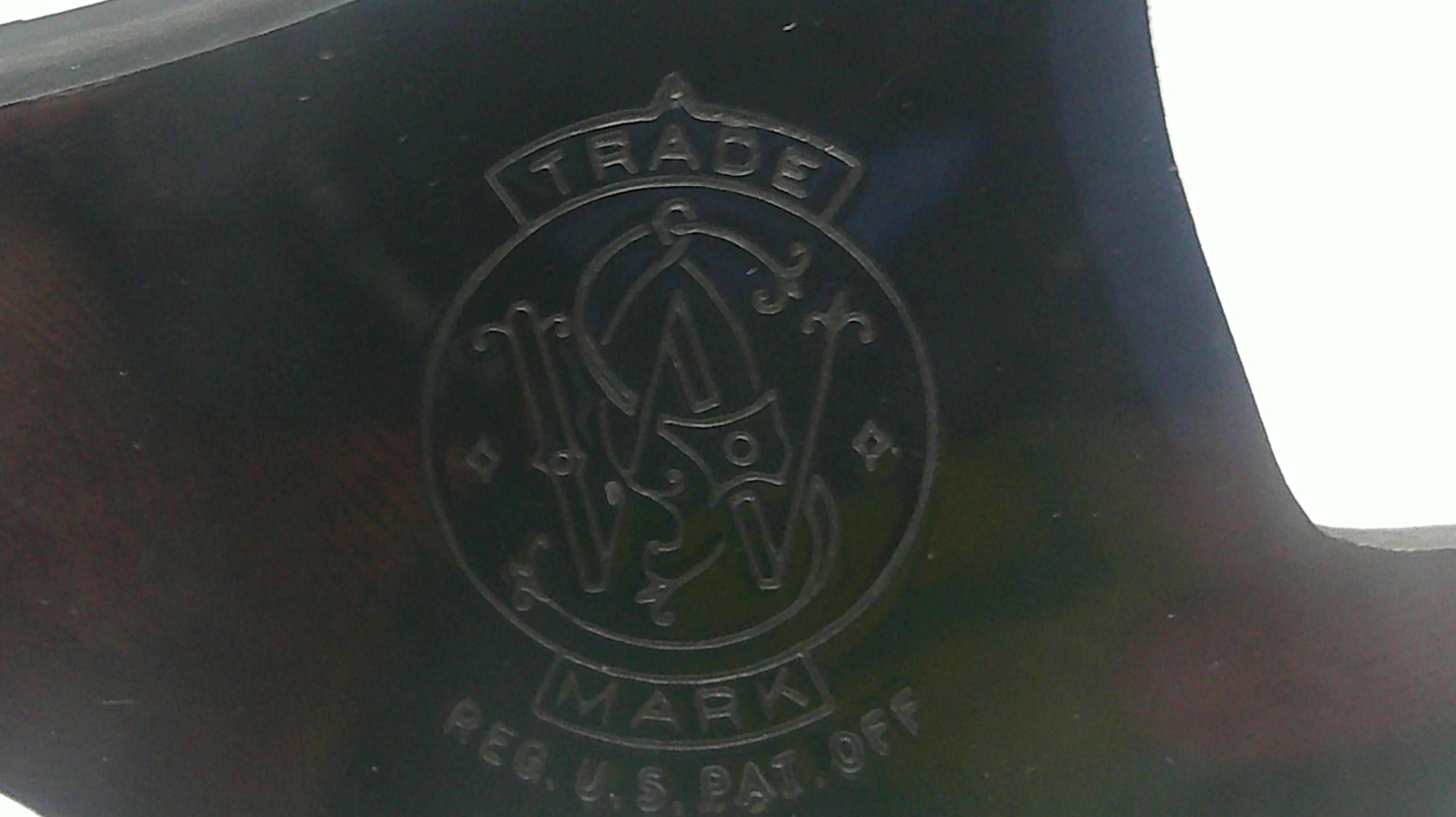 Close-up of a dark metallic or glossy black surface with an embossed circular logo reading TRADE MARK REG. U.S. PAT. OFF.