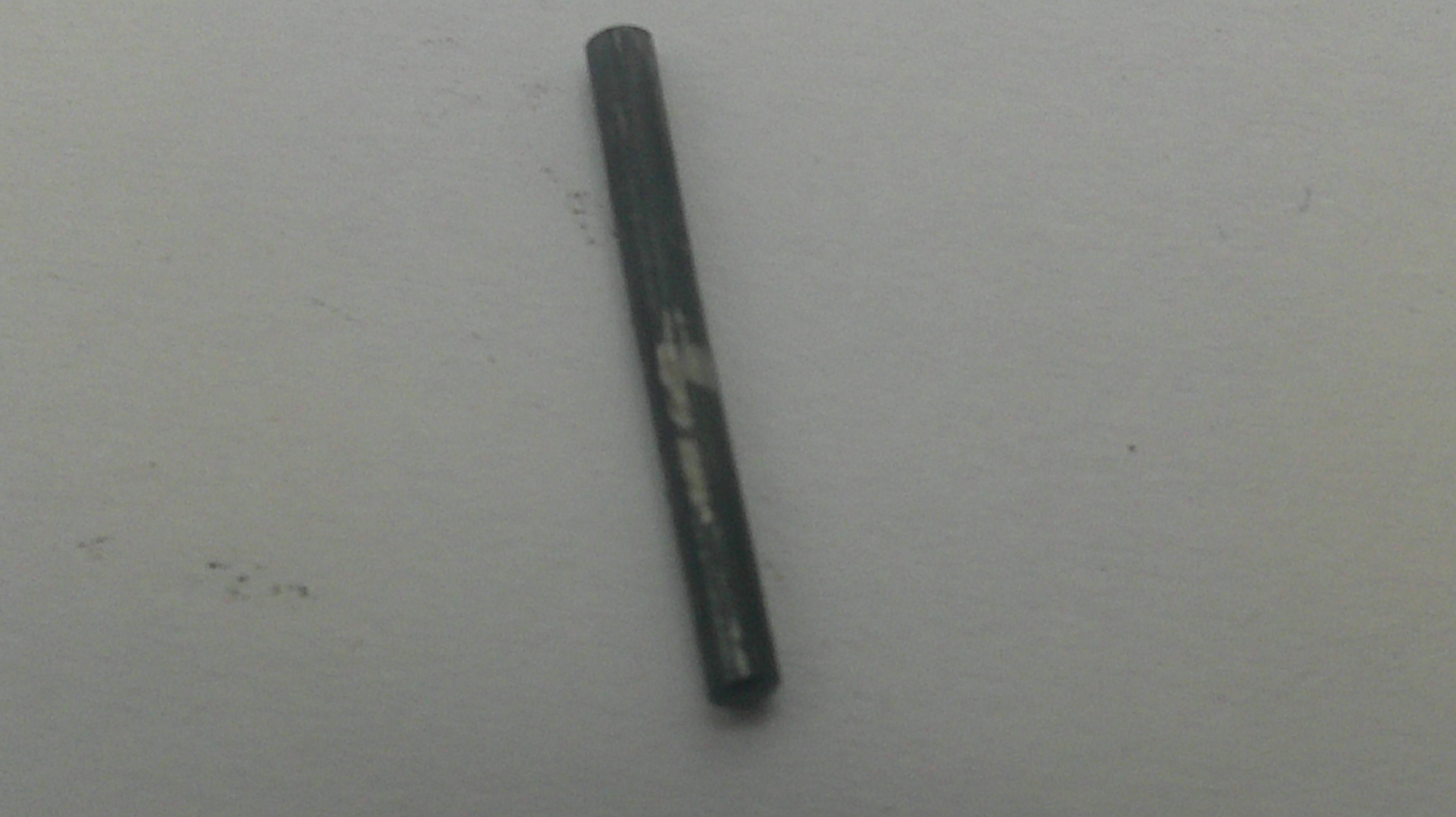 A single dark gray cylindrical rod or stick with a worn, scratched surface, placed vertically on a plain light gray background.
