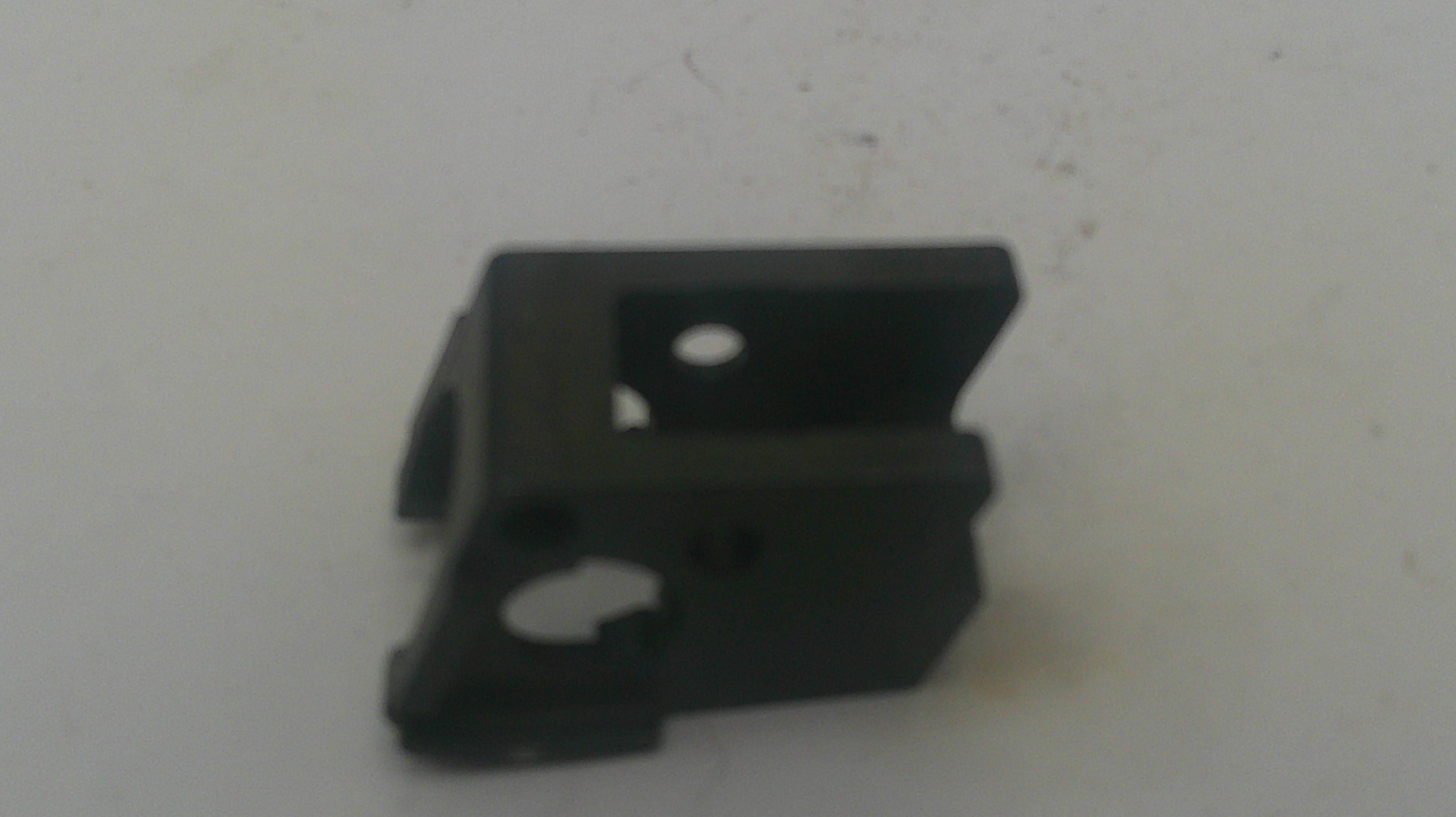 A small black plastic mounting bracket or clip with pre-drilled holes, shown on a plain off-white surface.