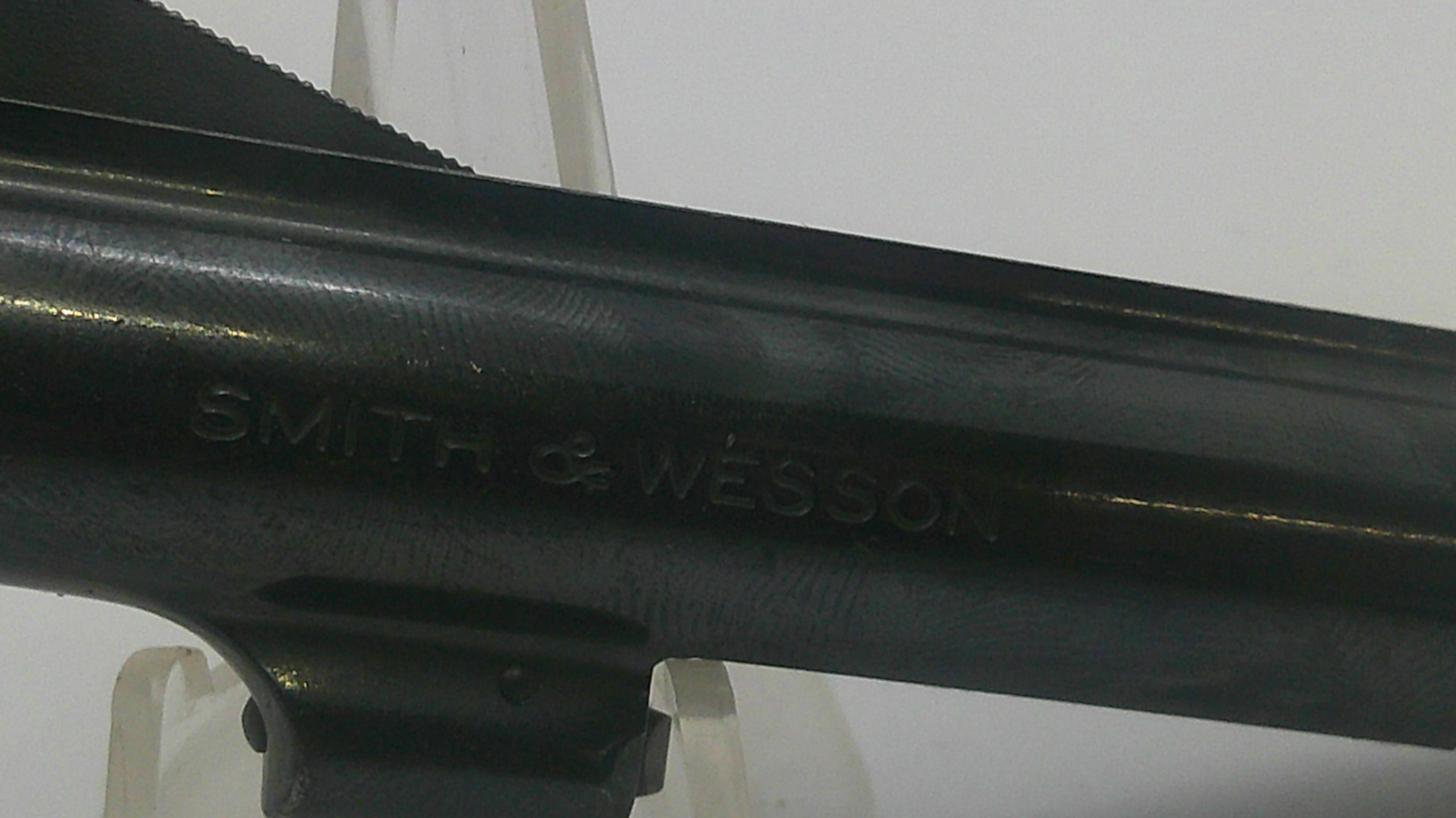 Close-up of a black metal firearm barrel with the embossed brand name 'SMITH & WESSON' visible against a light background.