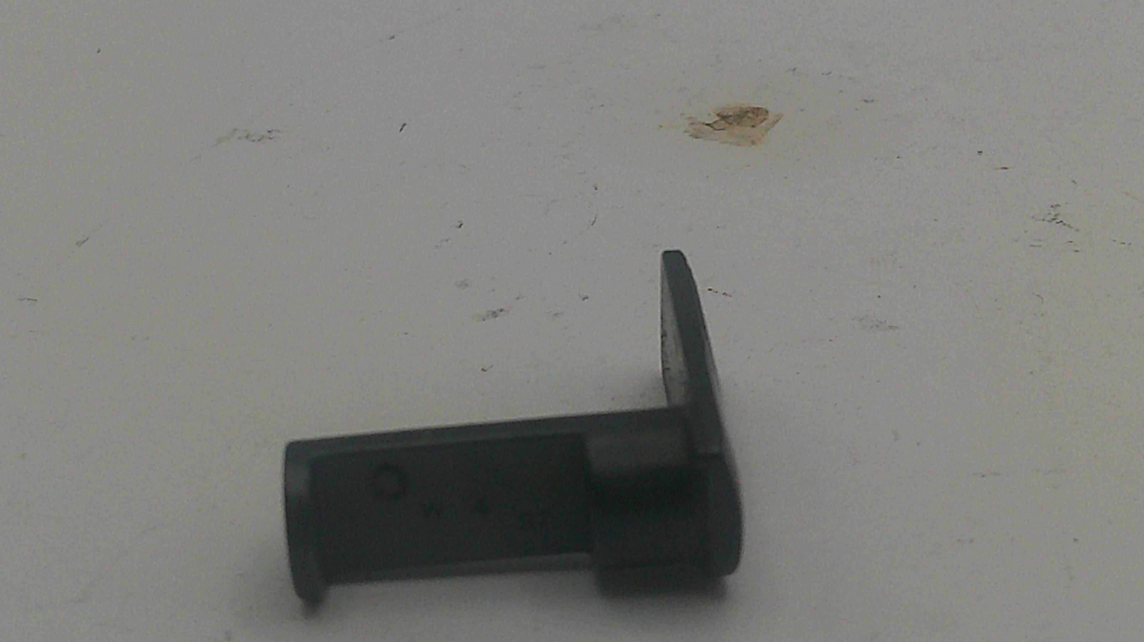 A small black plastic hardware component, possibly a latch or clip, lying on a light gray surface.