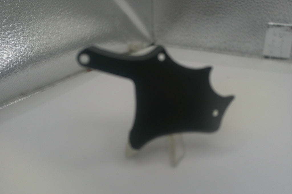 Black plastic component on a white surface with a metallic background
