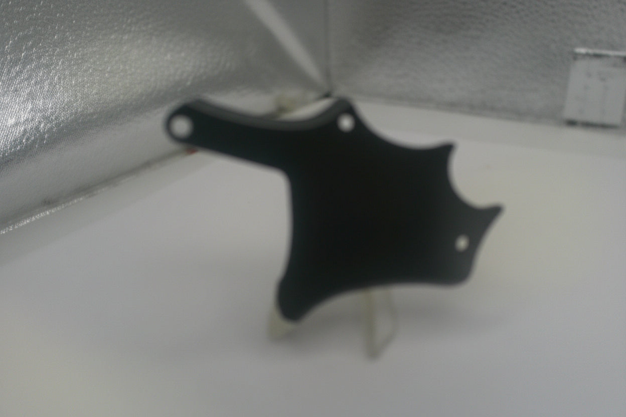 Black plastic component on a white surface with a metallic background