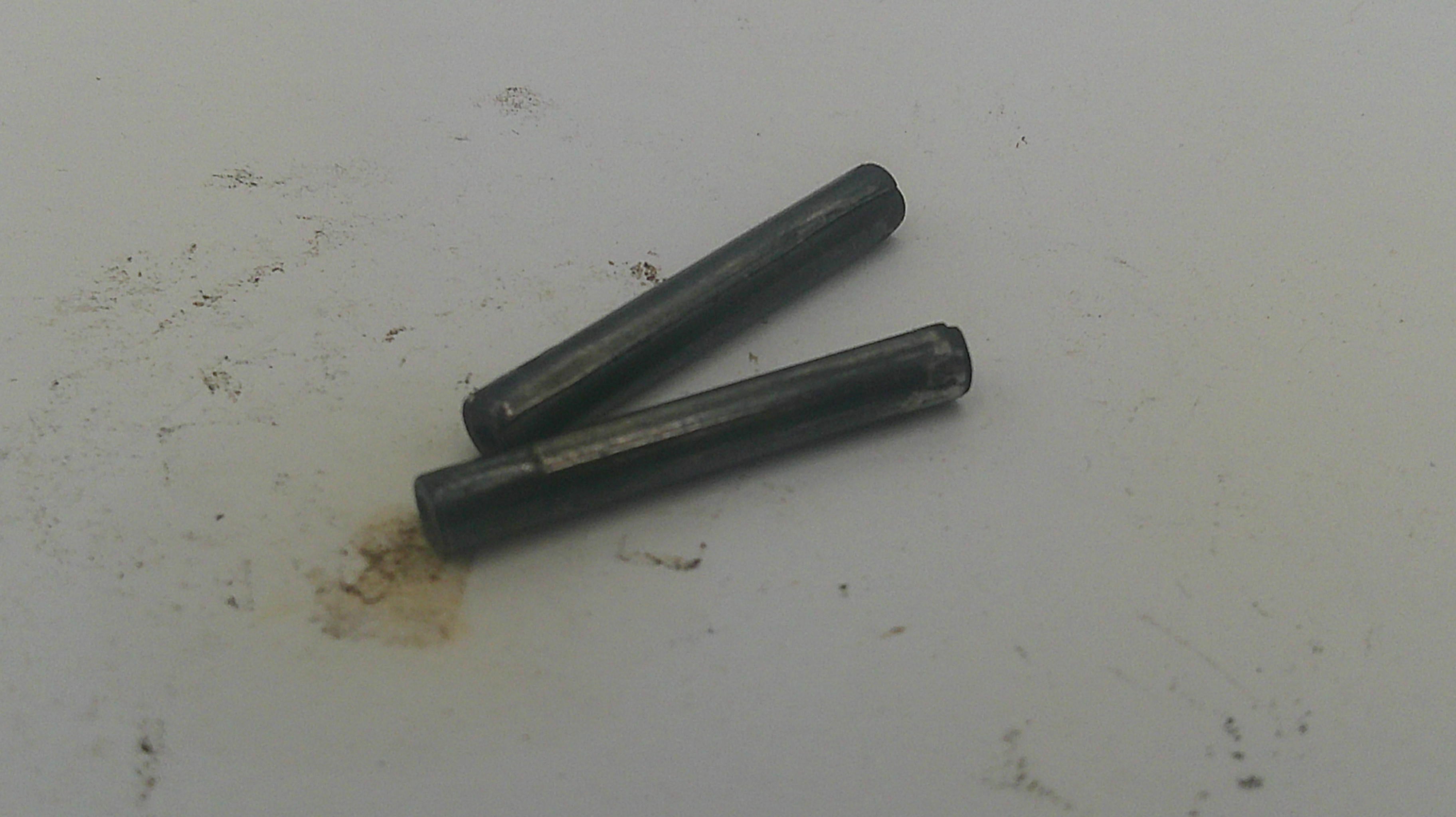 Two dark metallic cylindrical pins lying on a light gray surface.