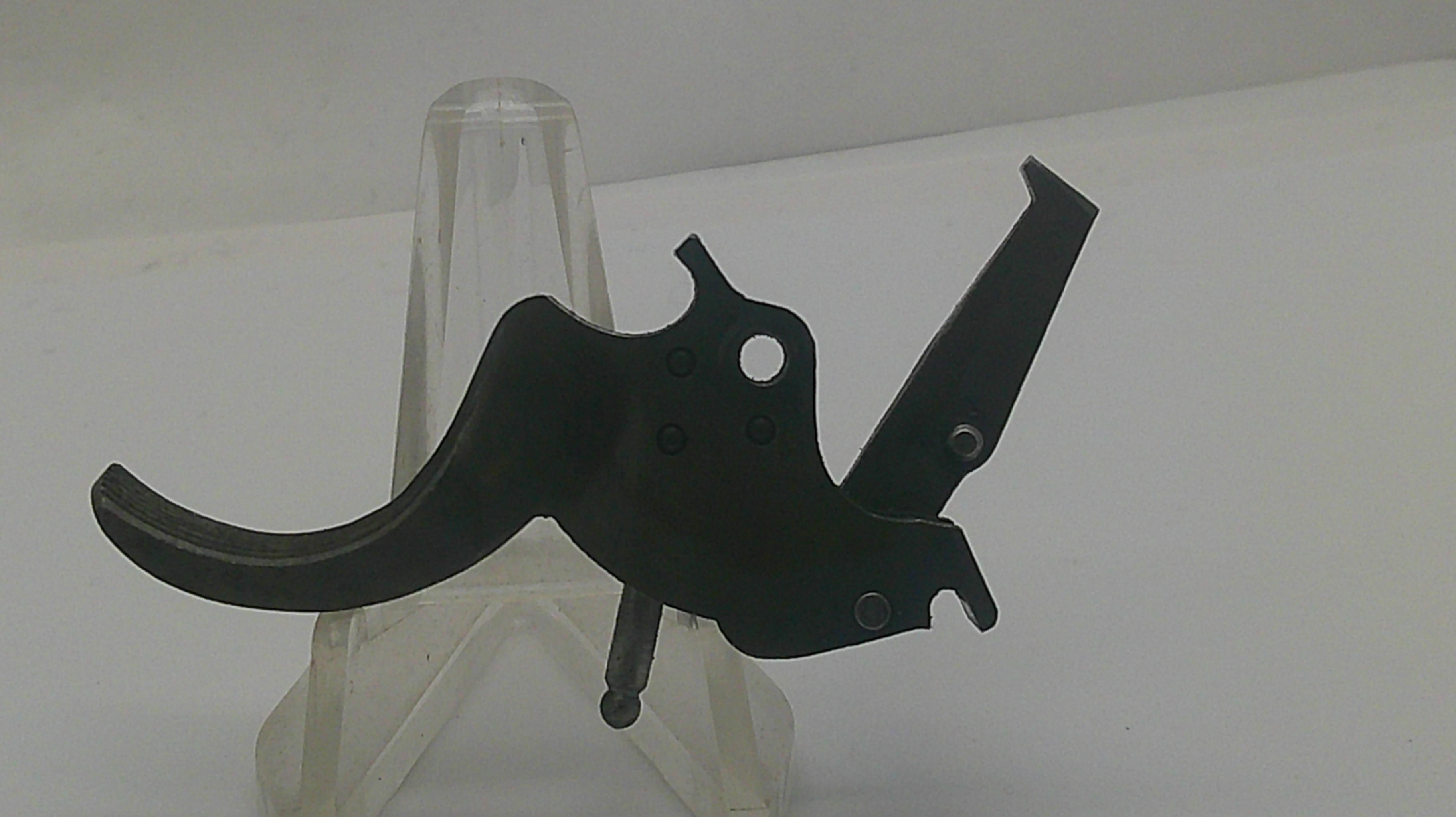 A black metal trigger assembly component displayed on a clear plastic stand against a plain white background.