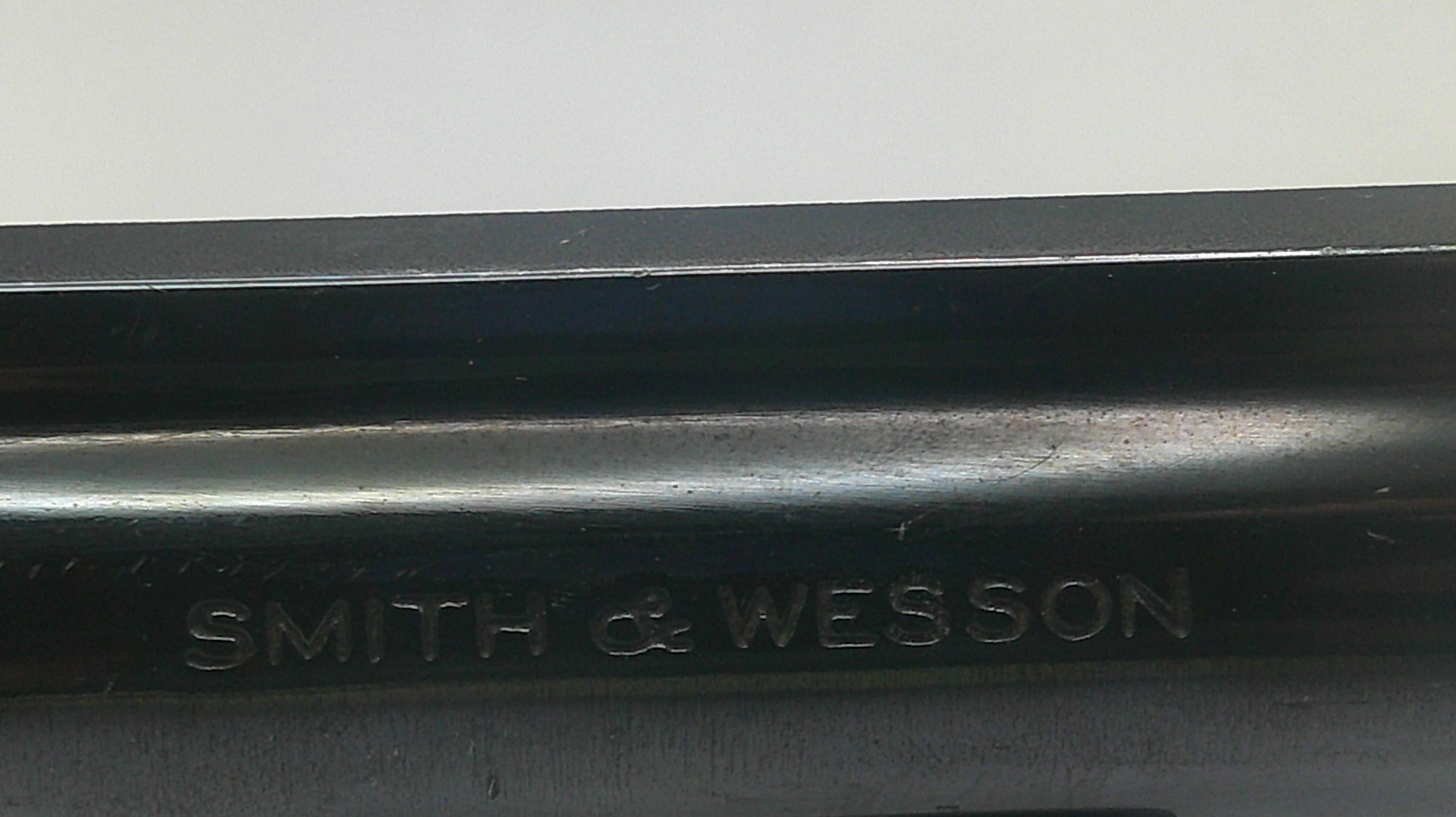 Close-up of a black metal surface with the embossed brand name 'SMITH & WESSON' visible against a light gray background.