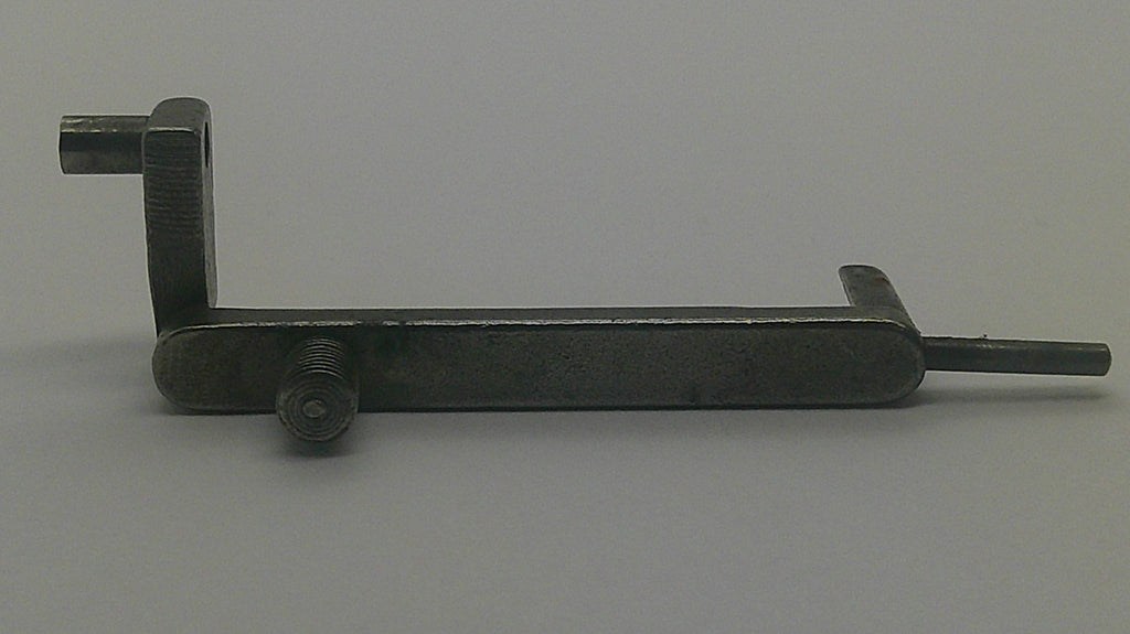 A dark metal latch or lock mechanism with a rectangular bolt, a vertical pin, and a long horizontal arm with a protruding pin, photographed on a plain light gray background.