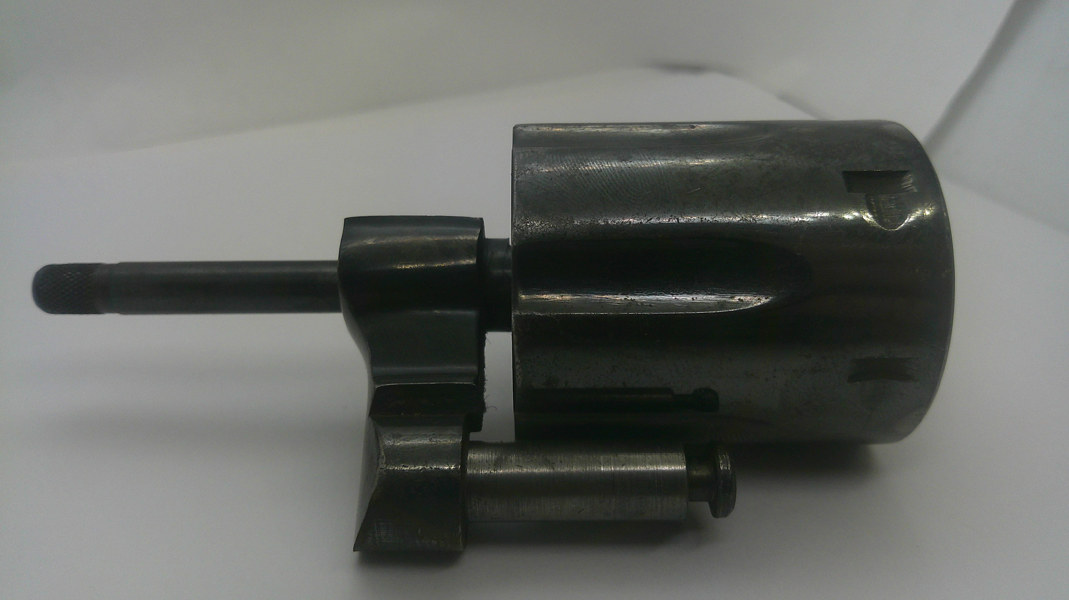 A dark metallic mechanical component or tool part with a cylindrical body and protruding shafts, photographed on a plain light background.