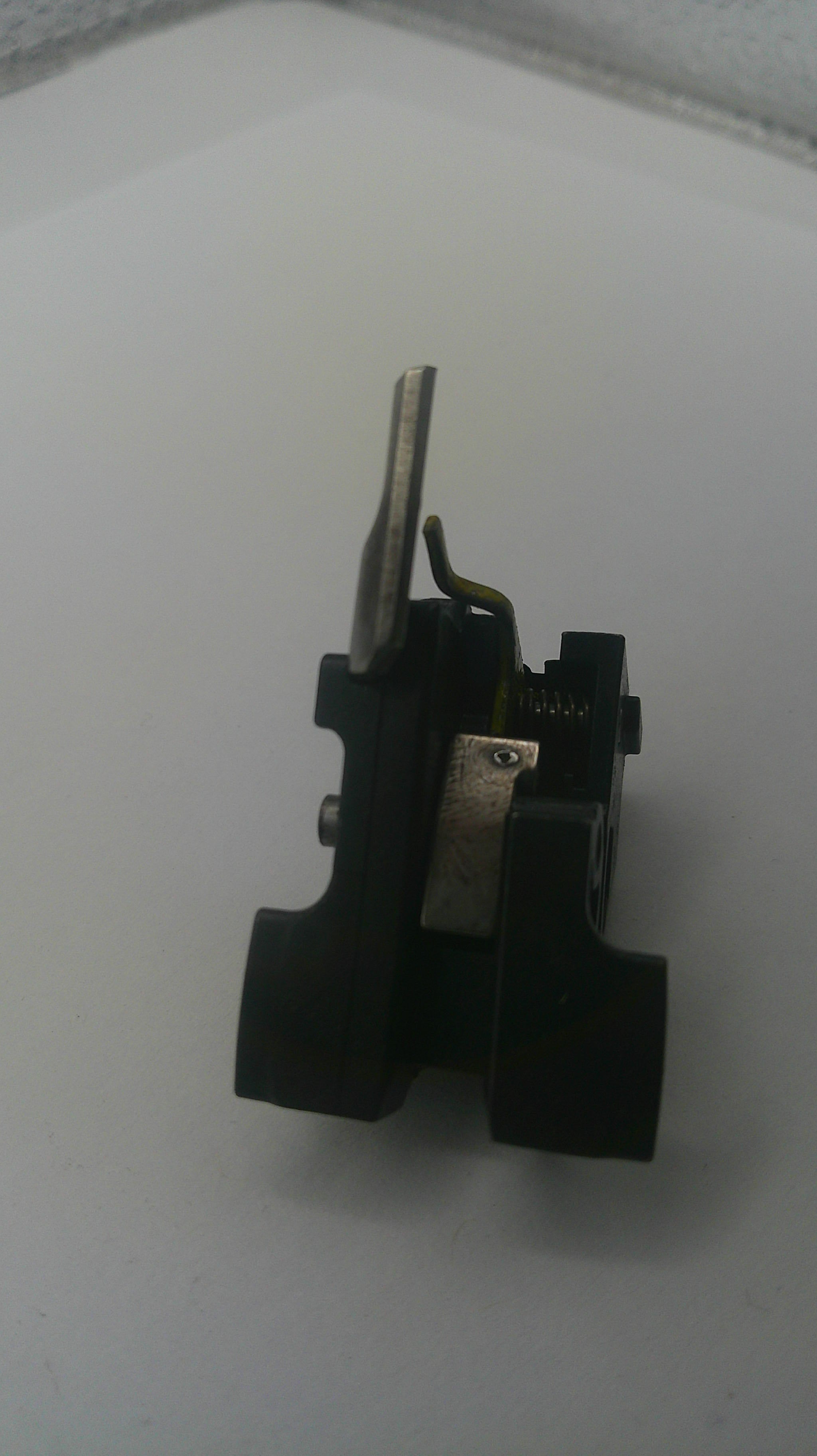 A small black plastic and metal mechanical component with a silver metal rod, photographed on a plain light background.