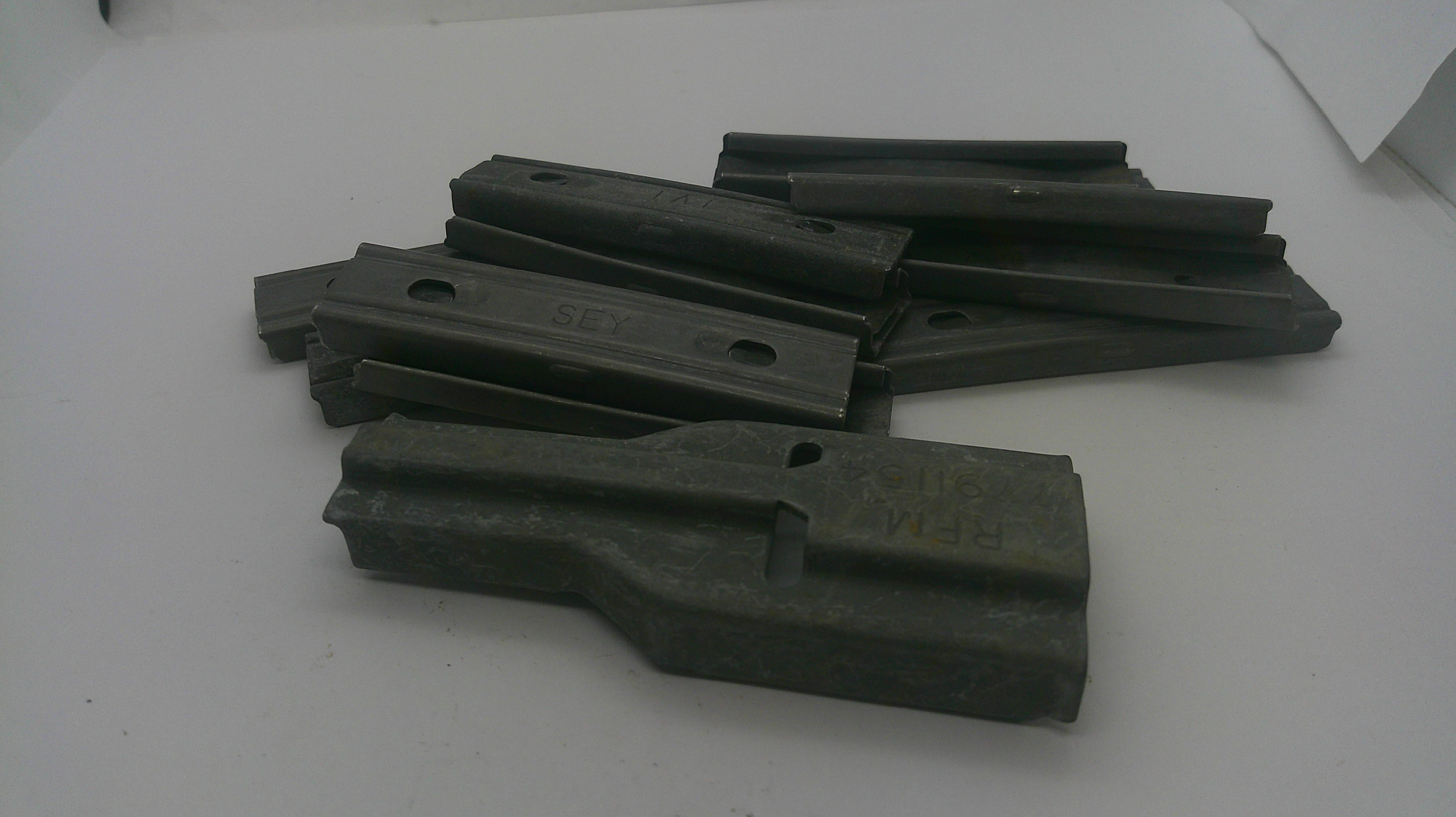 A pile of dark gray cast metal parts with pre-drilled holes, photographed on a plain white surface.