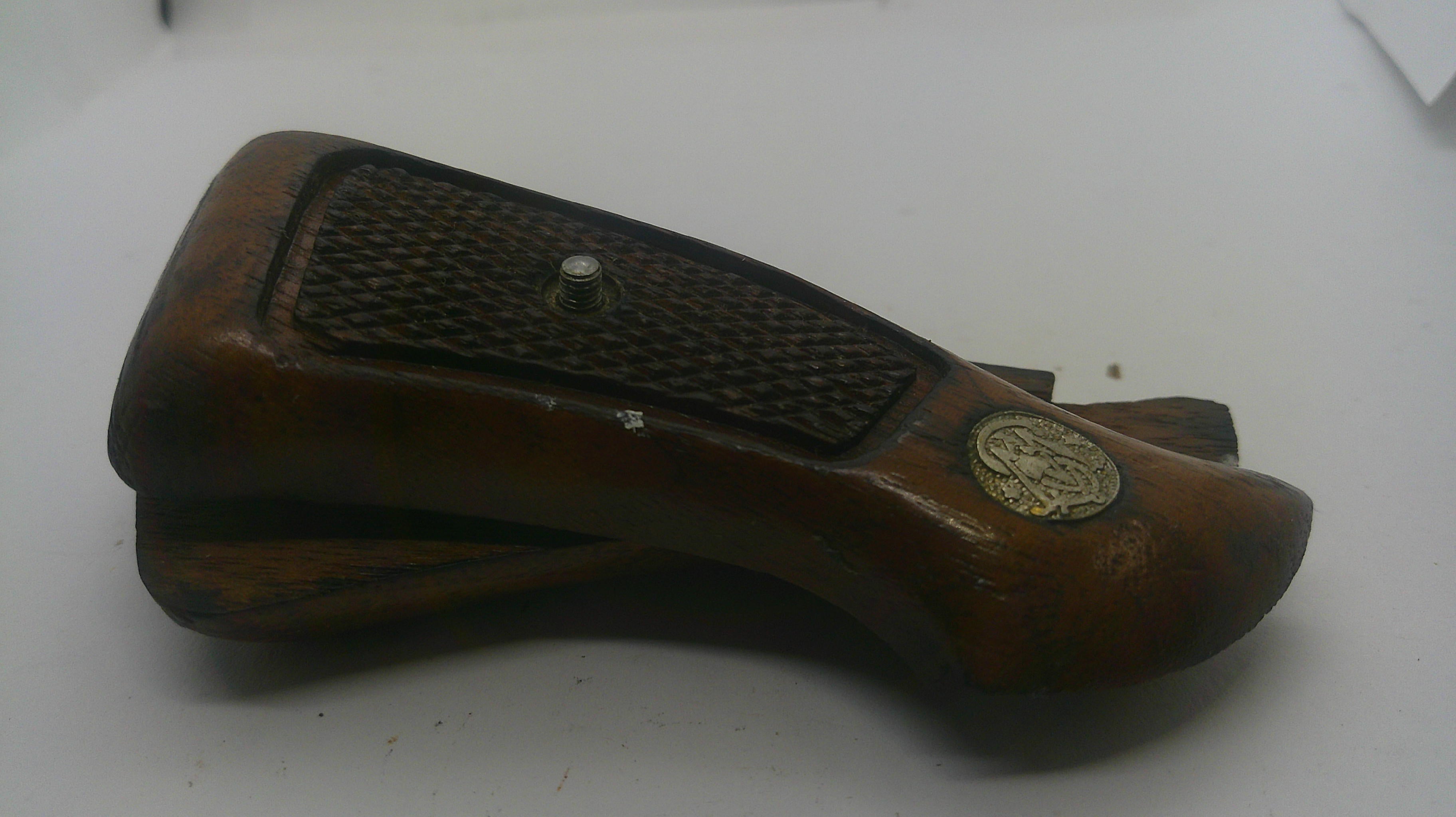 A vintage wooden object with a dark textured grip panel and a round brass emblem, photographed on a plain light background.