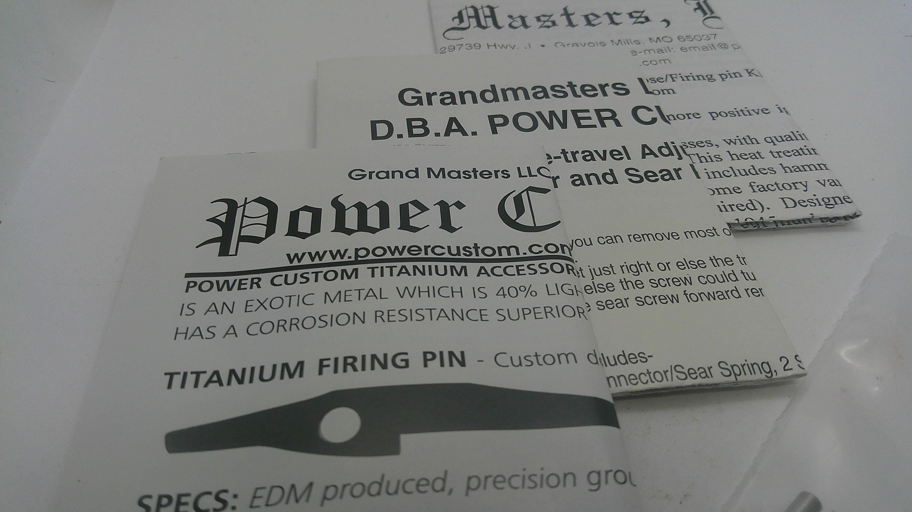 A close-up of printed product information cards for a titanium firing pin, including the text 'Power C', 'Grandmasters LK', 'D.B.