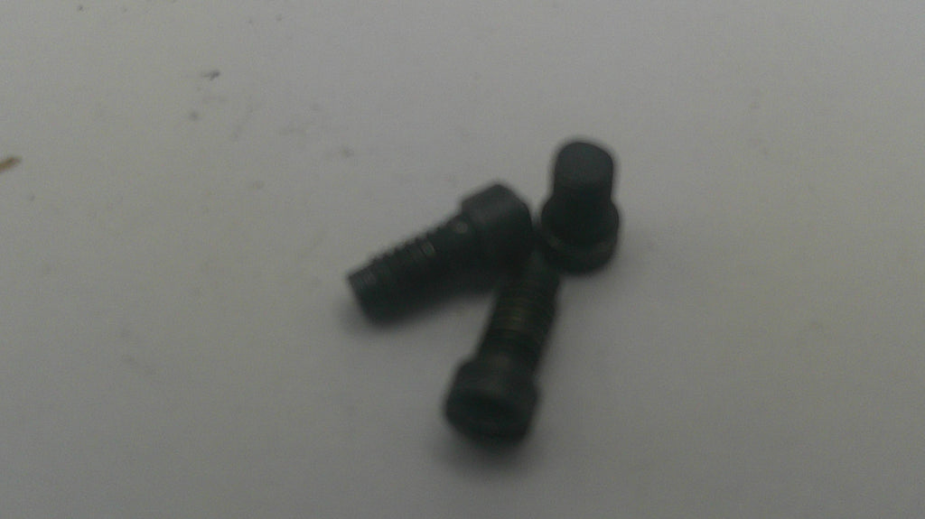 Two small black metal screws with flat countersunk heads on a plain light gray surface.