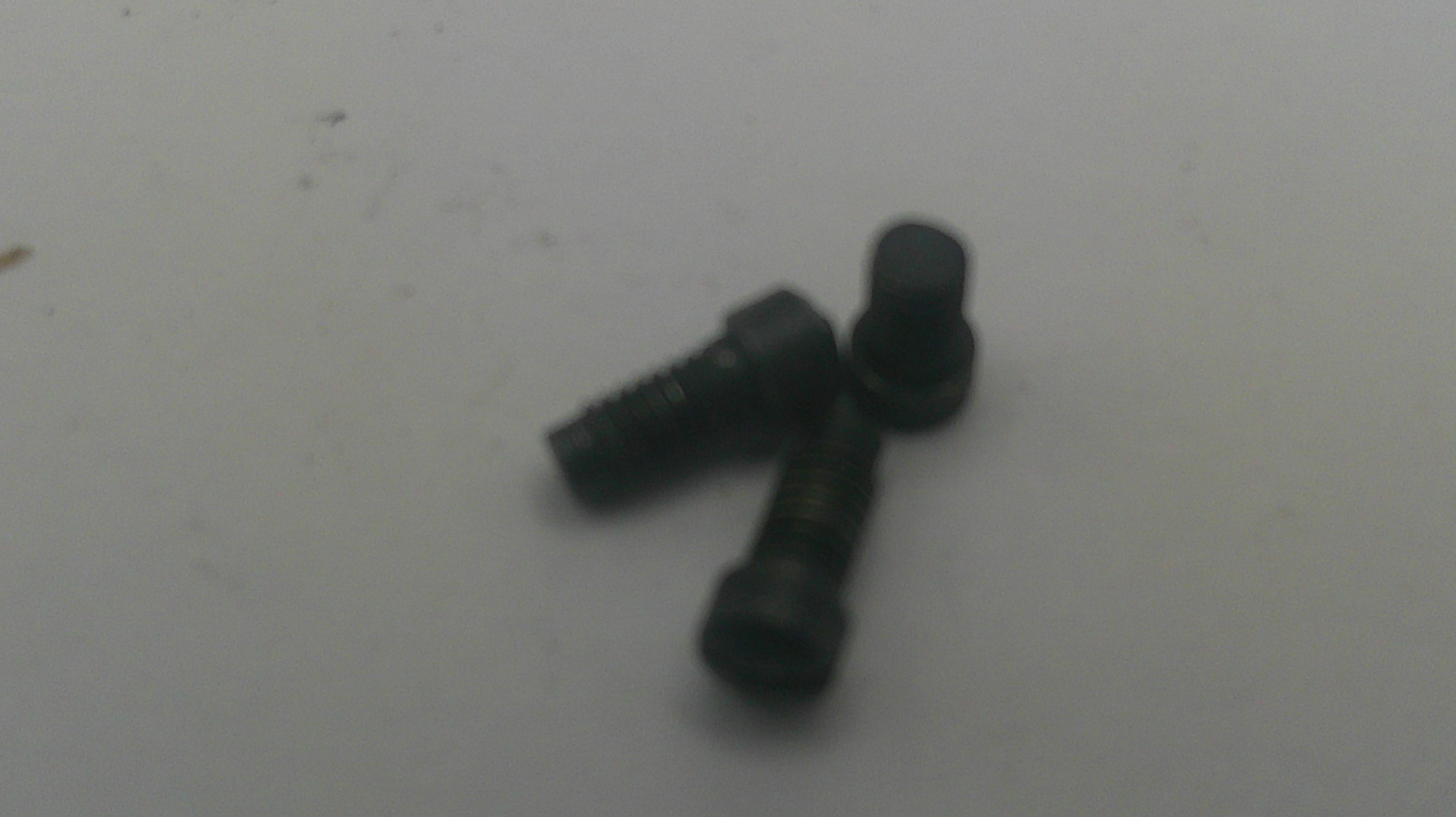 Two small black metal screws with flat countersunk heads on a plain light gray surface.