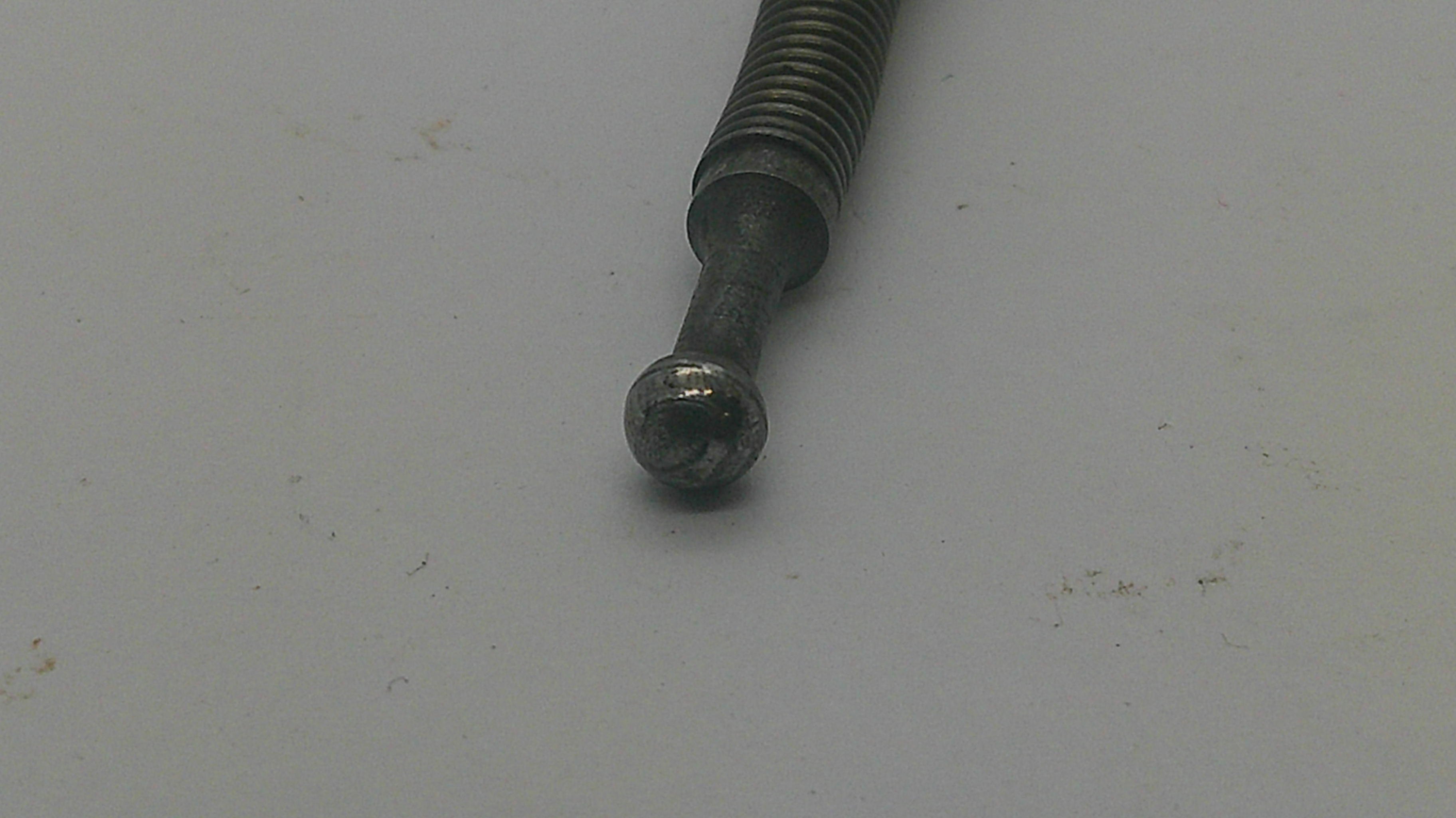 A close-up of a dark metal threaded rod or bolt with a spherical ball end, resting on a plain light gray surface.