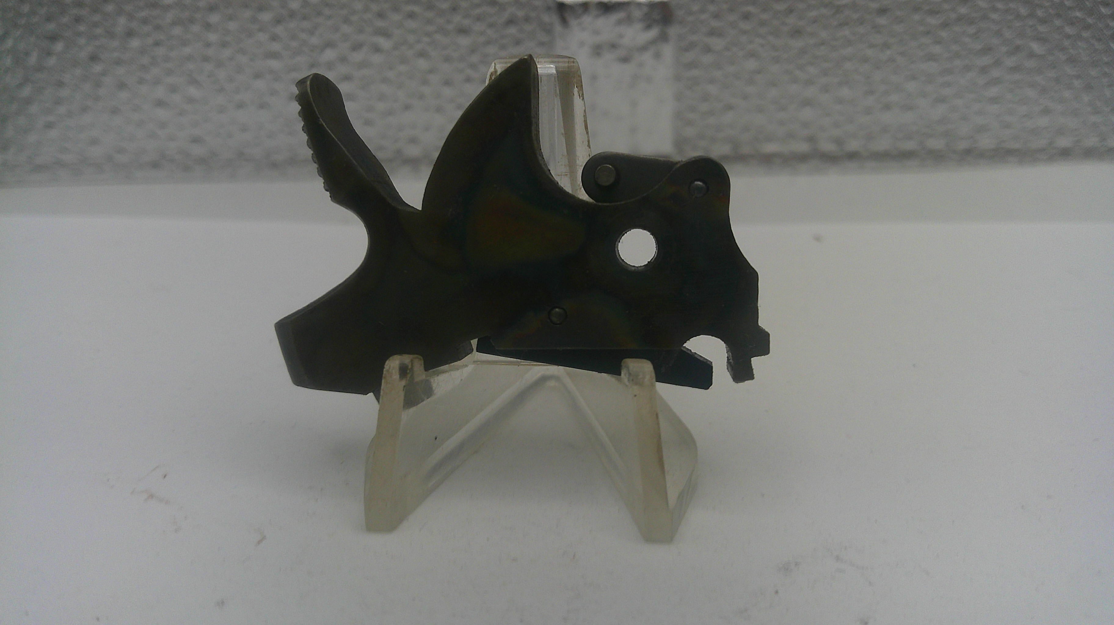 Black metal component on a white stand against a textured gray background