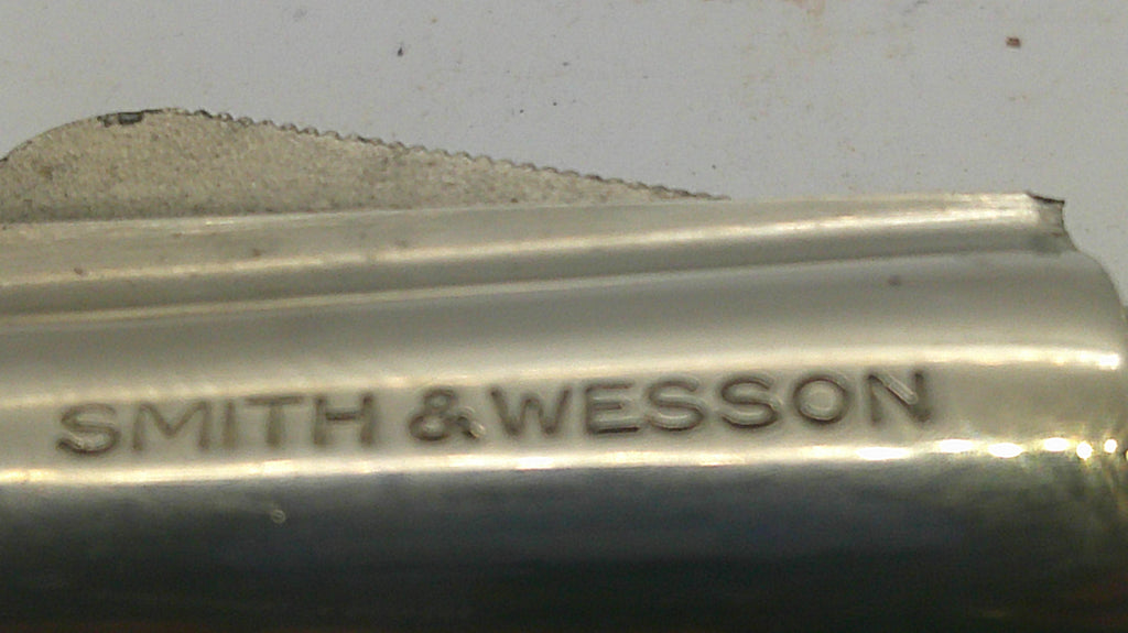 Close-up of a metallic cylindrical object with the brand name 'SMITH & WESSON' engraved on it, against a light gray background.