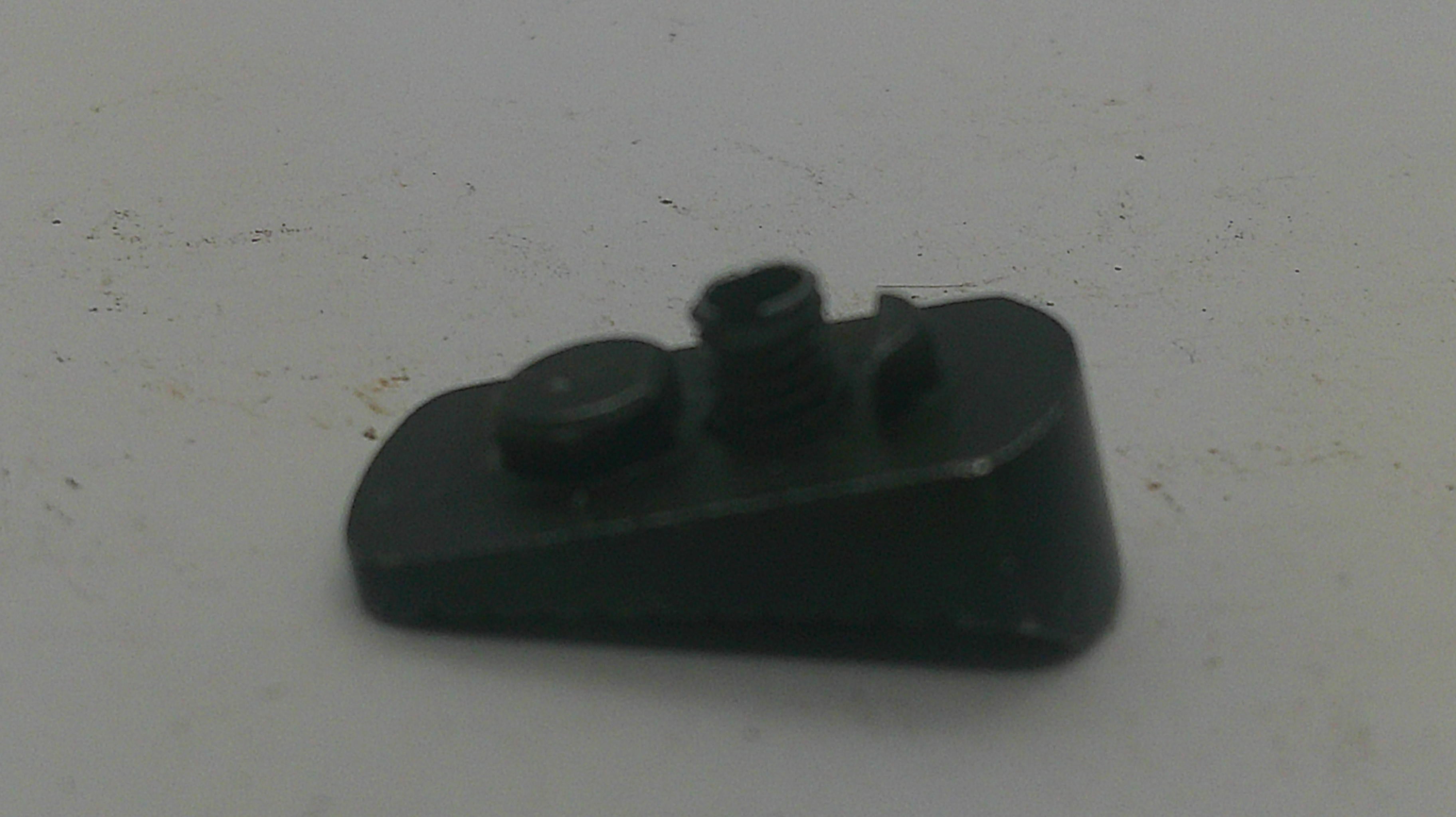 A small black plastic component with a threaded hole and a circular protruding tab, photographed on a plain off-white surface.