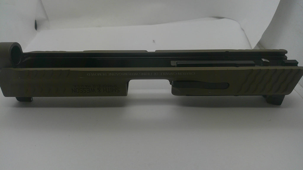 An olive drab green metal receiver or slide component with black rubber boots and a black textured grip, photographed against a plain white background.