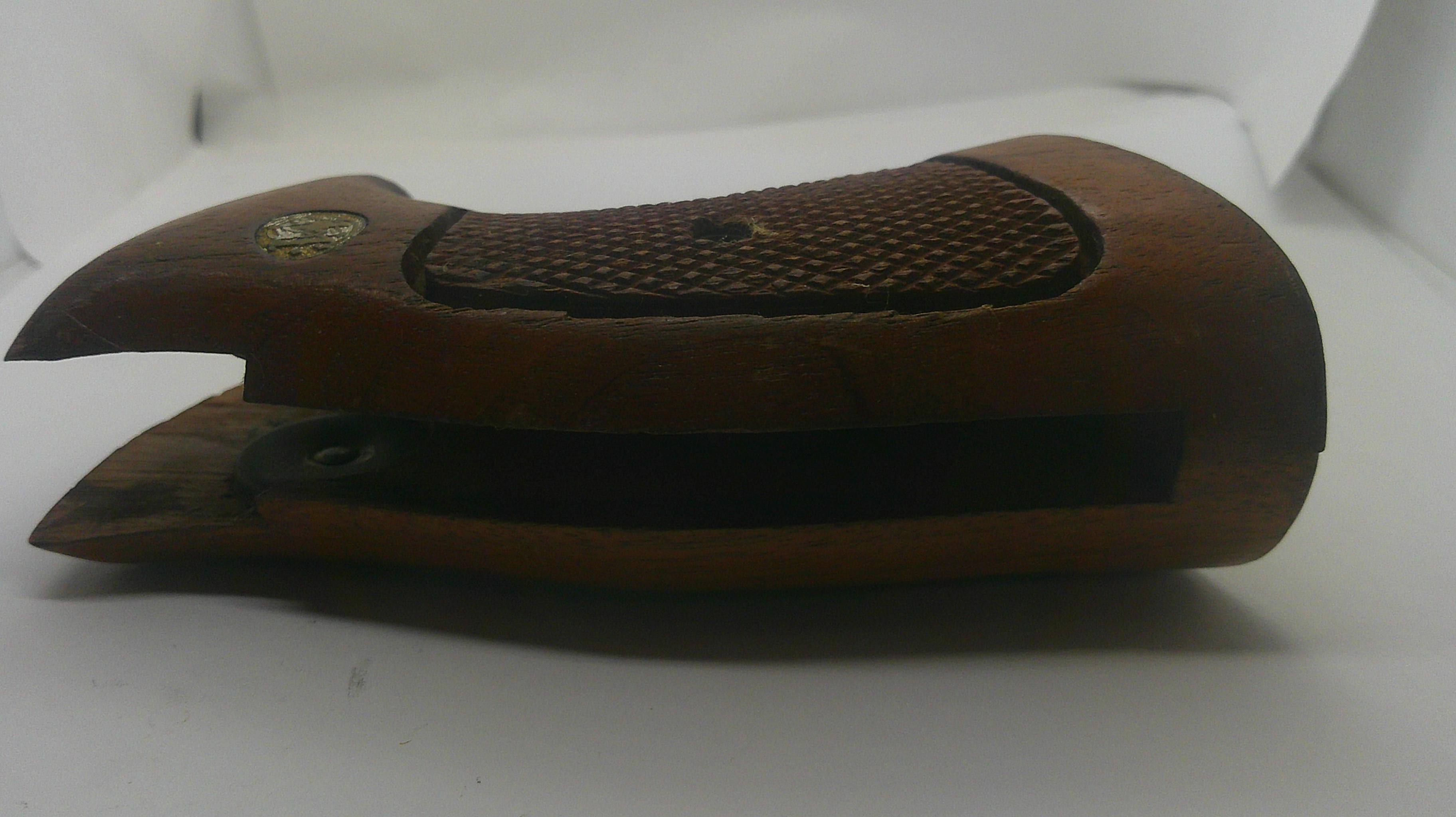 A wooden gun stock or receiver cover made of medium brown wood with a textured grip panel and a small brass emblem, shown on a white background.
