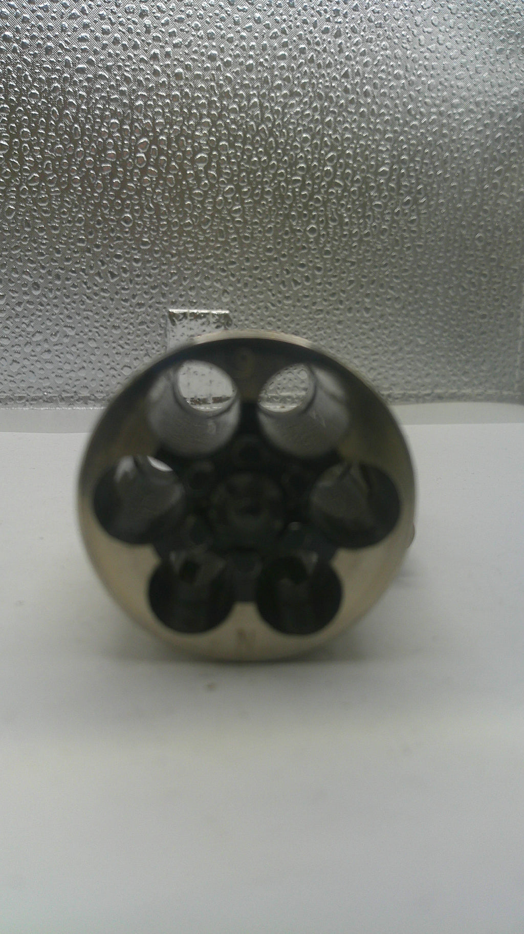 Close-up of a metallic cylindrical object with multiple holes on a textured surface.