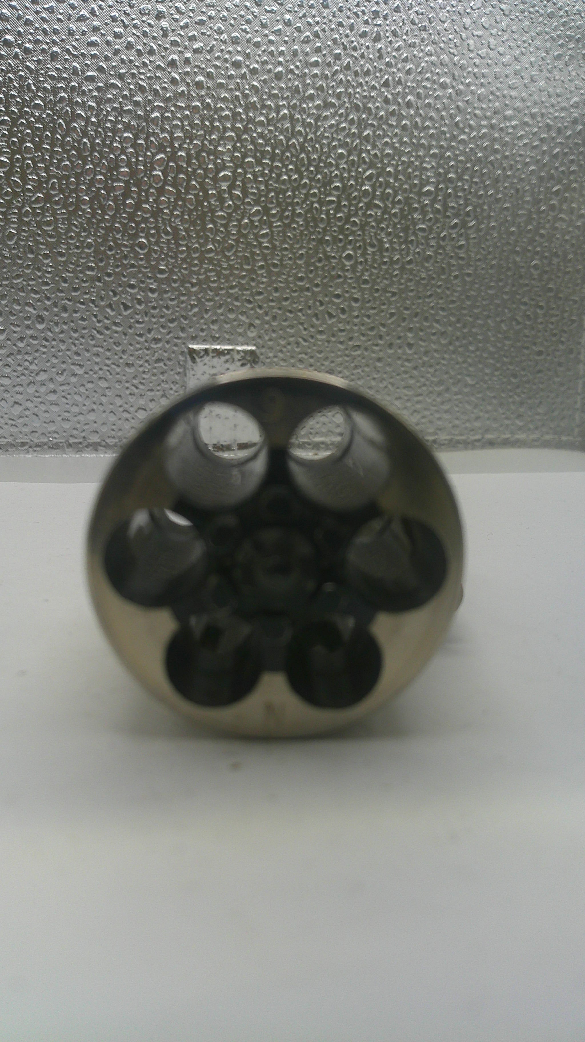 Close-up of a metallic cylindrical object with multiple holes on a textured surface.