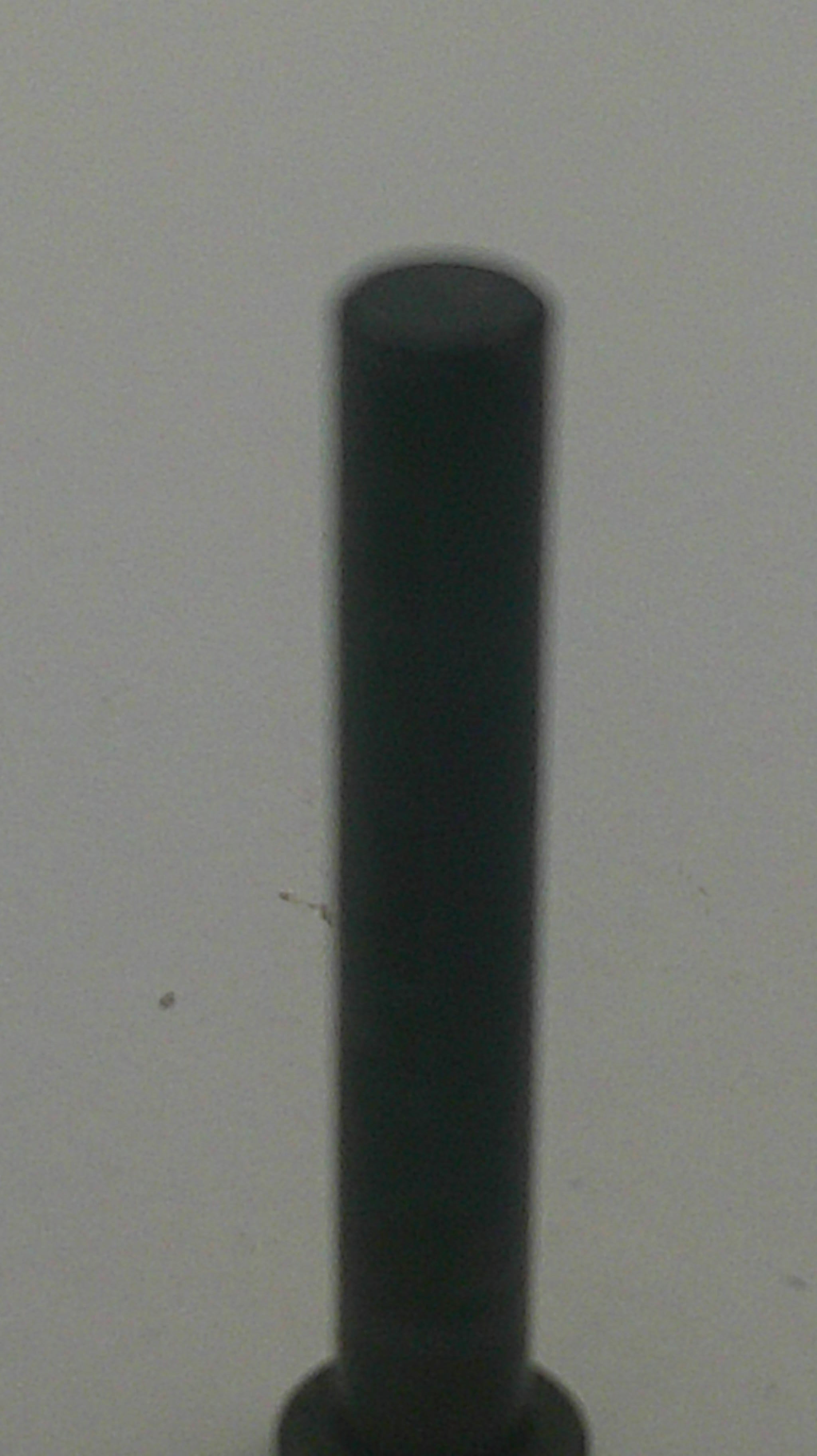 A close-up of a dark gray or black cylindrical rod or stick extending horizontally against a light gray background.