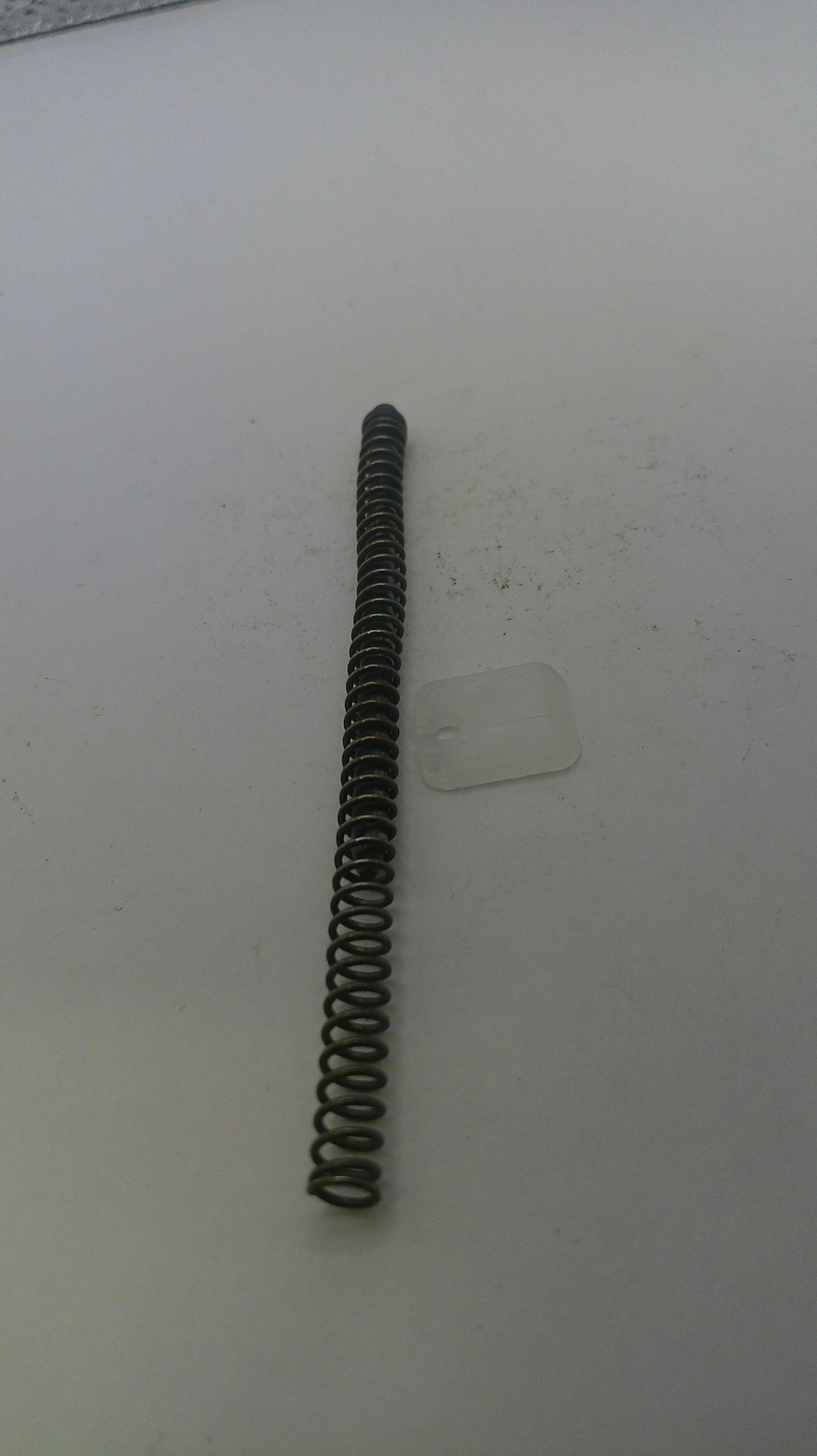 Coiled spring on a white surface with a clear plastic piece underneath