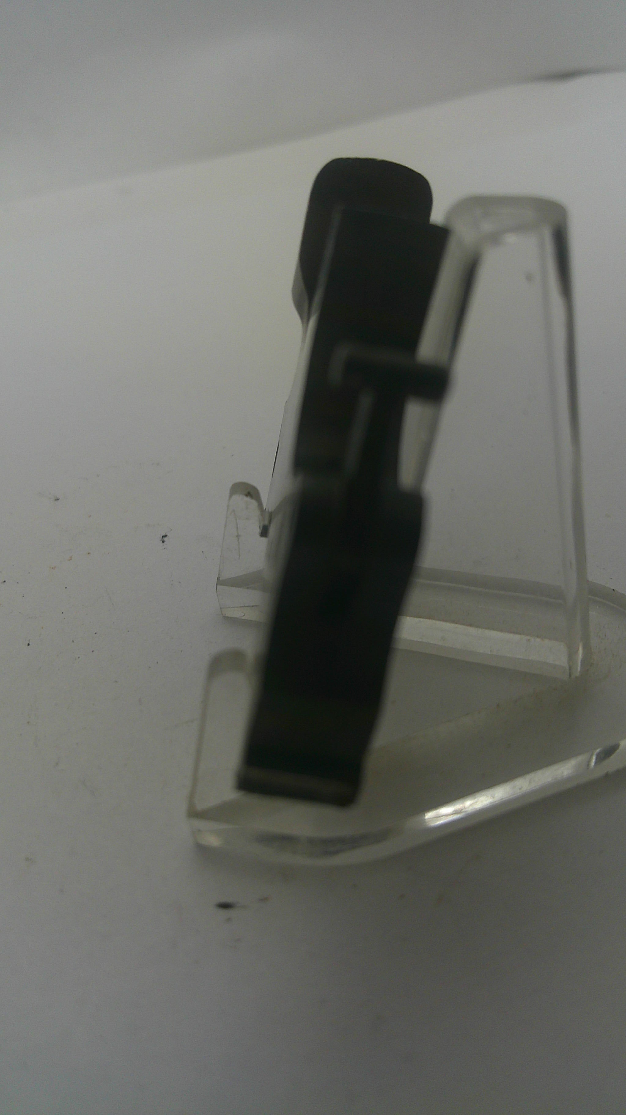 A close-up of a clear plastic eyeglass stand holding a pair of black-framed eyeglasses against a plain light background.